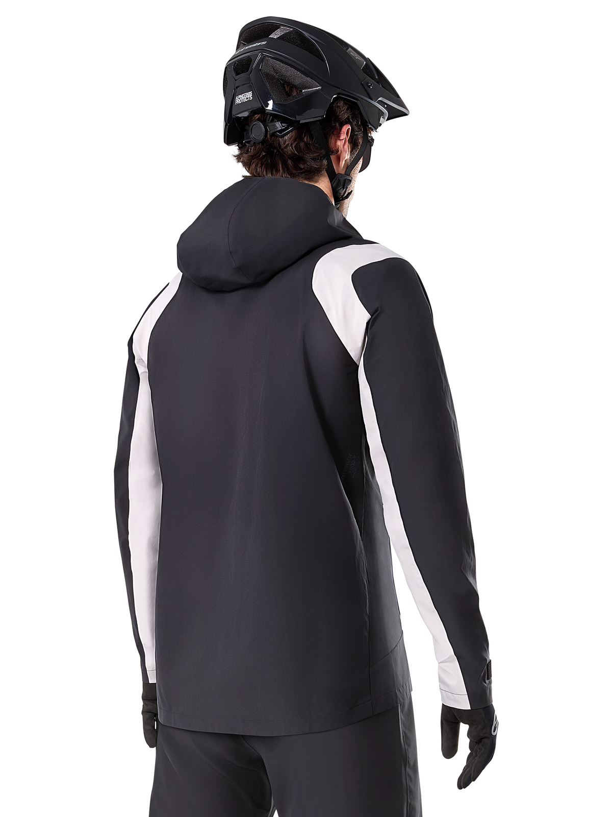Alpinestars A-Dura Rain Jacket, Mountain Bike Rain Jacket, Black with white sleeve panels, rear view of rider wearing a black MTB helmet and gloves, technical 2.5-layer waterproof construction, mountain biking apparel