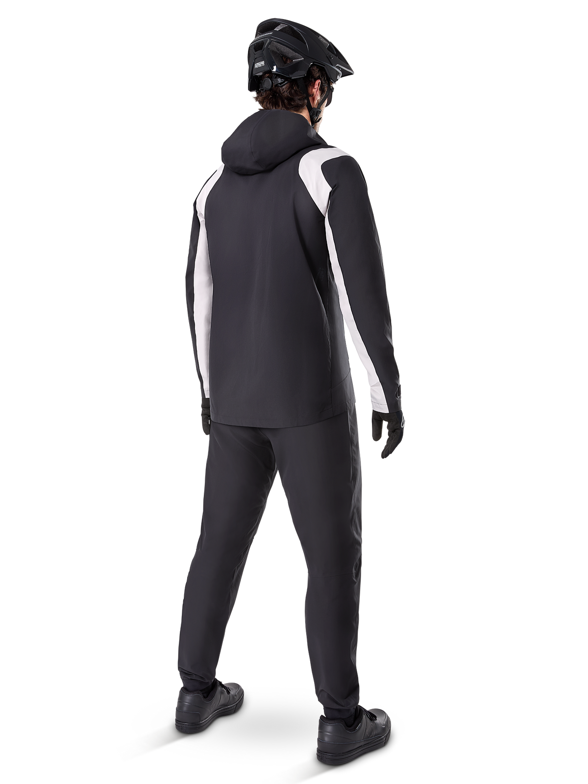 Alpinestars A-Dura Rain Jacket, back view of a male cyclist wearing the black and white waterproof MTB jacket, matching black cycling pants, black helmet, and gloves, technical gear for mountain biking in wet conditions.