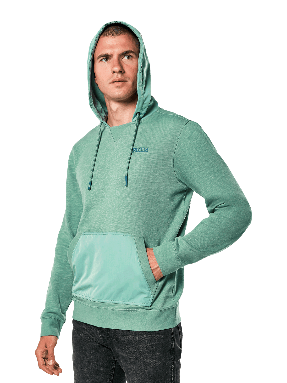 Alpinestars Rooted Hoodie, zielona bluza z kapturem z dzianiny French terry typu slub, kieszeń typu kangurka, małe logo STARS na piersi, model z założonym kapturem i ręką w kieszeni, streetwear inspirowany sportami motorowymi