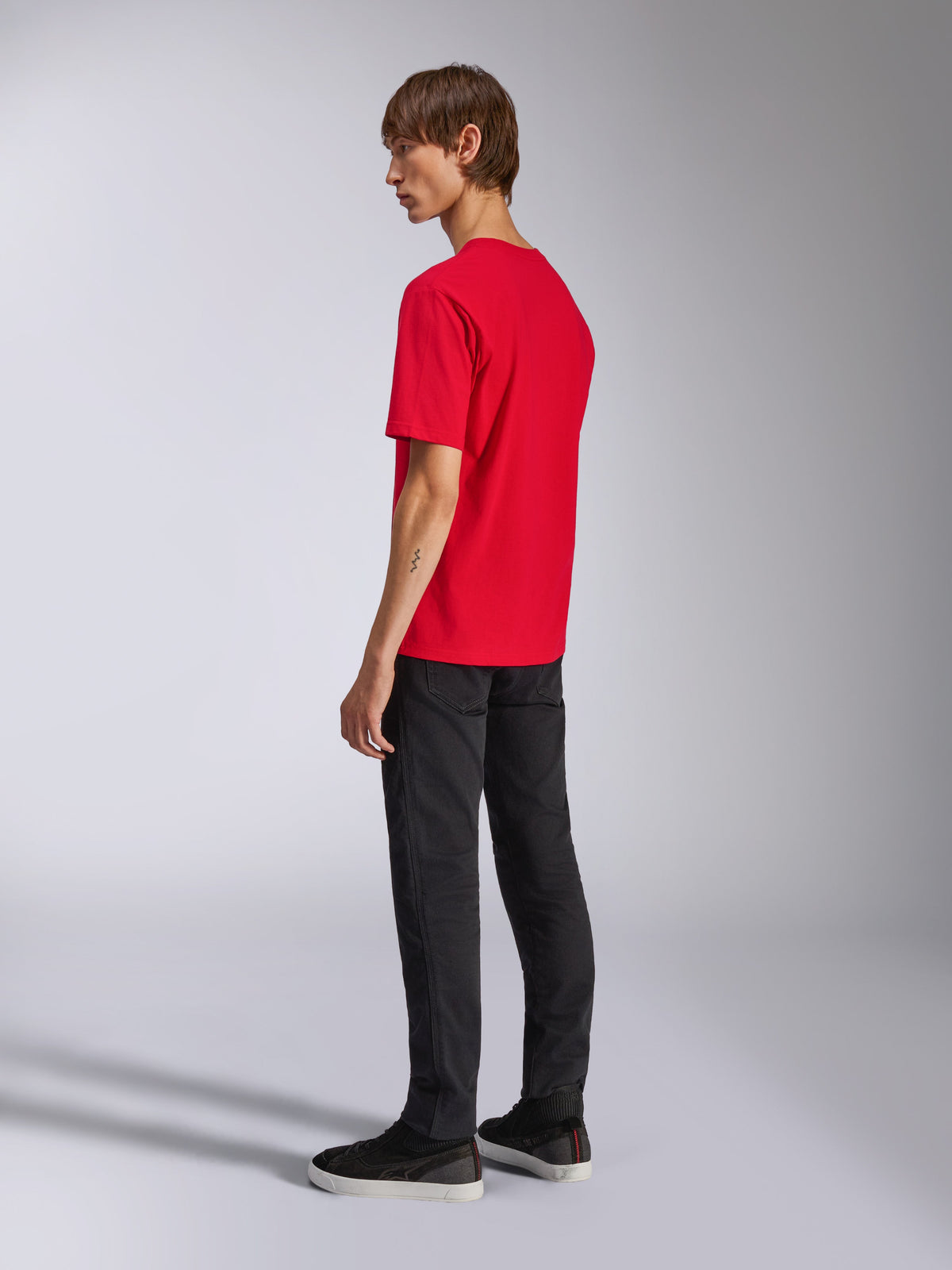 Alpinestars Ageless Shadow CSF Tee, koszulka z krótkim rękawem, czerwona, widok z tyłu na modelu, noszona z czarnymi spodniami i sneakersami, codzienna odzież streetwear inspirowana sportami motorowymi