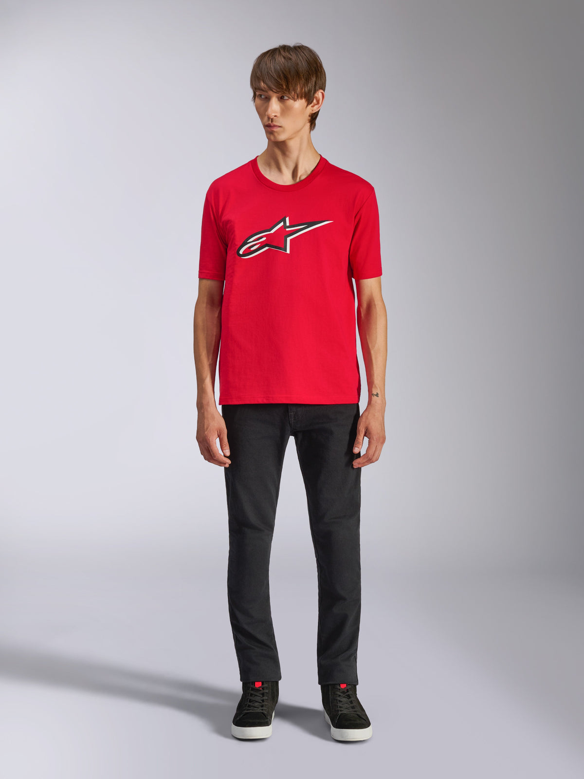 Alpinestars Ageless Shadow CSF Tee, koszulka z krótkim rękawem, czerwona, logo Ageless z przodu z białą i czarną obwódką, noszona przez modela w czarnych spodniach i sneakersach, casualowa odzież uliczna w stylu motorsport