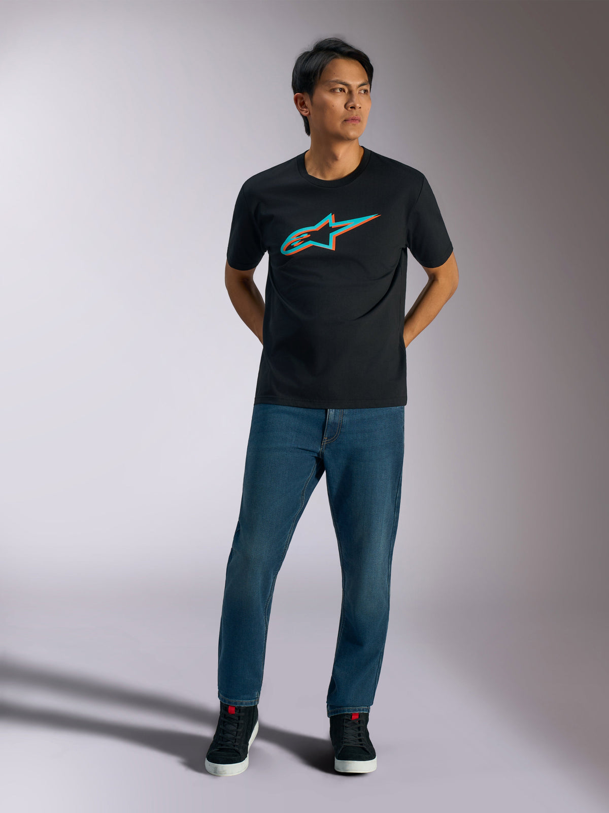 Alpinestars Ageless Shadow CSF Tee, Short Sleeve T-Shirt, Black, Turquoise and Orange Ageless shadow logo on chest, worn by model with blue jeans and black shoes, casual motorsport streetwear