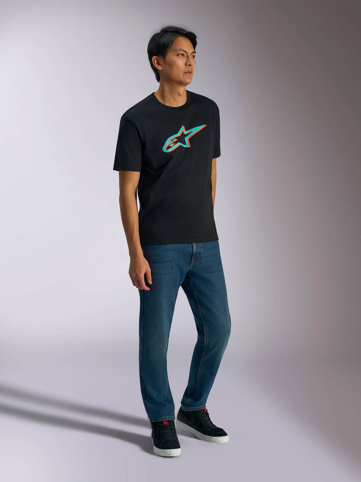 Alpinestars Ageless Shadow CSF Tee, Short Sleeve T-Shirt, Black with Turquoise and Orange Shadow Logo, worn by male model with blue jeans and black sneakers, casual motorsport-inspired streetwear
