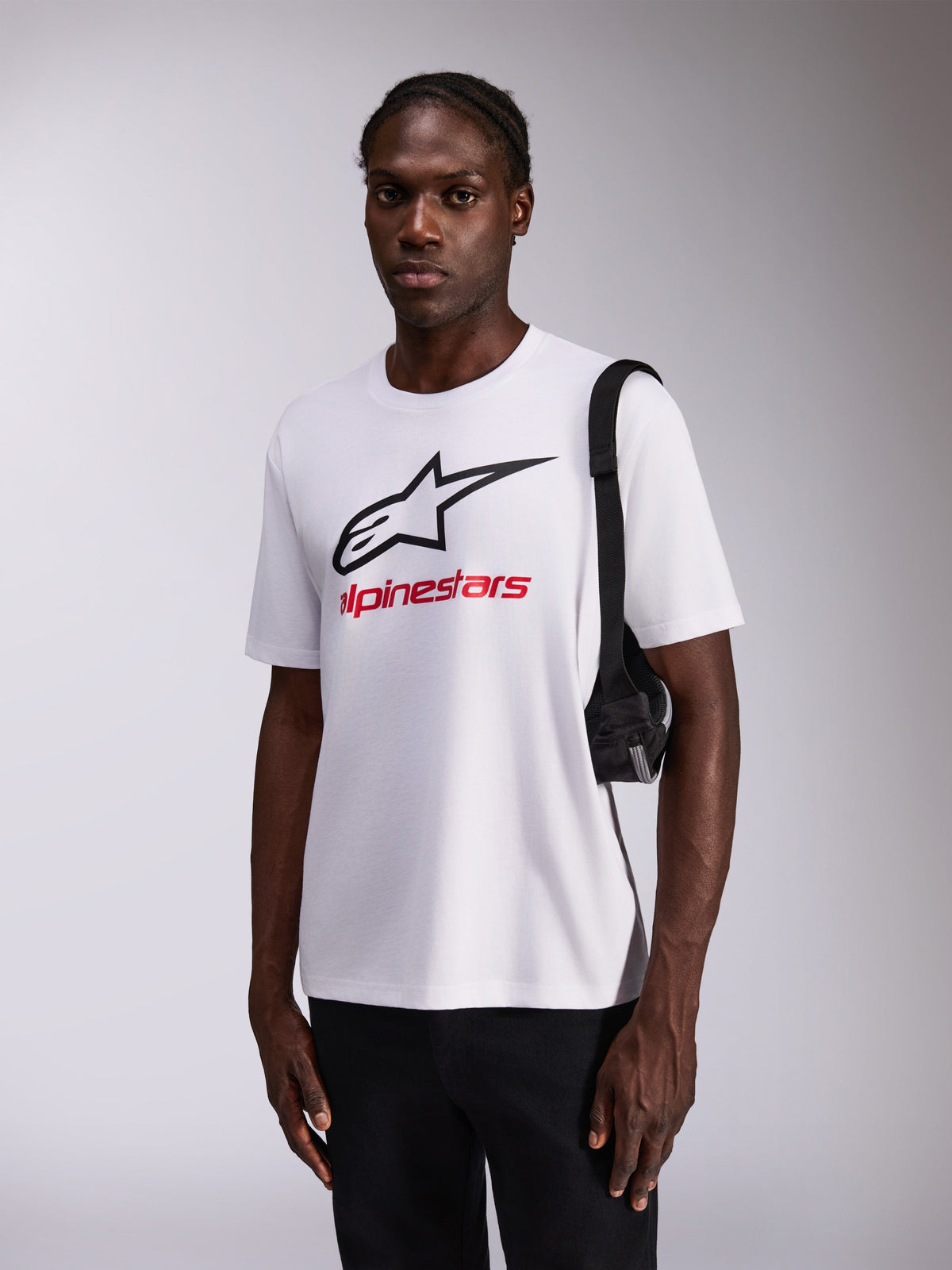 Alpinestars Always 2.0 CSF Tee, Short Sleeve T-Shirt, White with large Black Star Logo and Red branding, worn by model with black pants and shoulder bag, casual motorsport-inspired streetwear