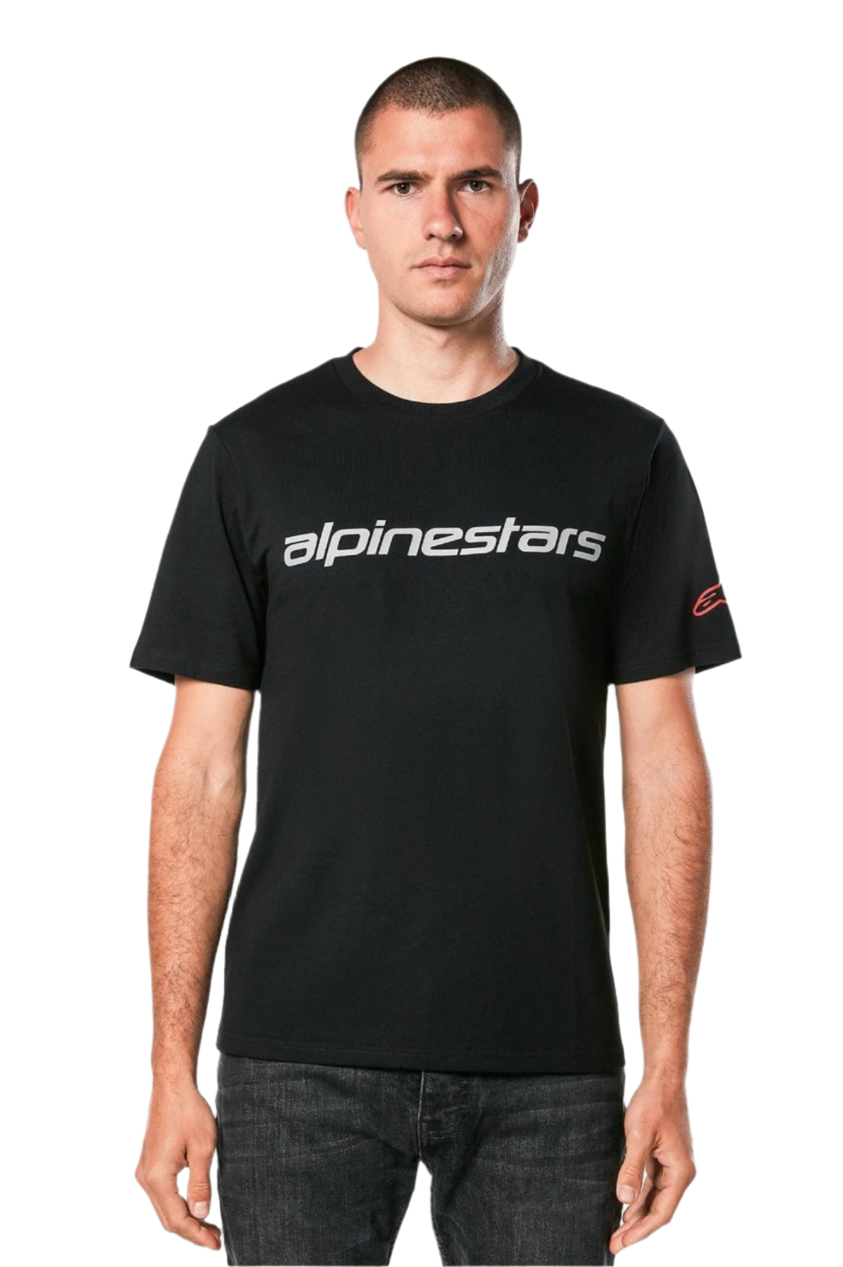 Koszulka Alpinestars Linear Wordmark 2.0 CSF, t-shirt z krótkim rękawem, czarny, szary linearny znak słowny na klatce piersiowej i czerwone logo Ageless na rękawie, noszona przez modela z ciemnymi jeansami, casualowy streetwear inspirowany sportami motorowymi