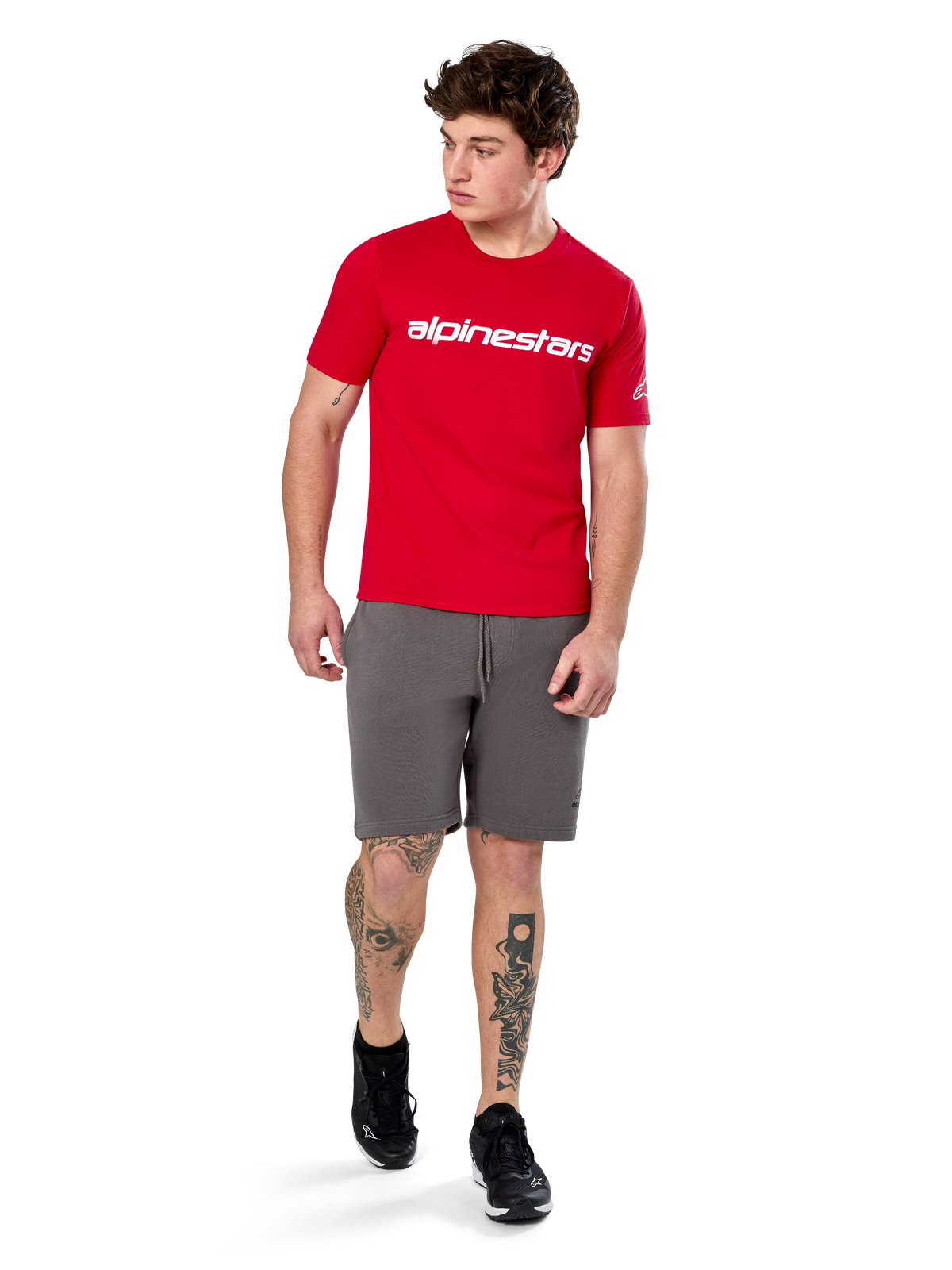 Alpinestars Linear Wordmark 2.0 CSF Tee, koszulka z krótkim rękawem, czerwona z białym logotypem na piersi, noszona przez modela w szarych szortach i czarnych sneakersach, codzienna odzież uliczna inspirowana sportami motorowymi