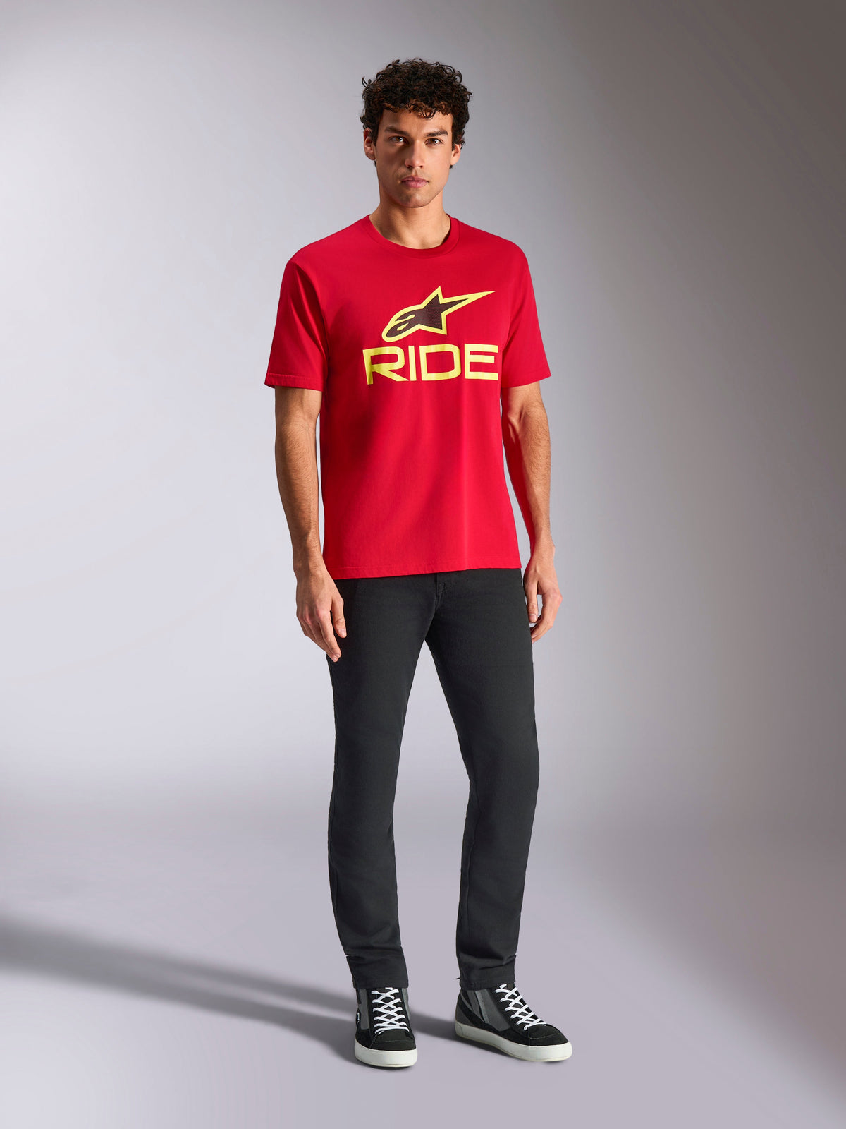 Alpinestars Ride 4.0 CSF Tee, koszulka z krótkim rękawem, czerwona z jaskrawożółtym logo Alpinestars Star i napisem Ride, noszona przez modela z czarnymi spodniami i sneakersami, casualowa odzież sportowa motorsport