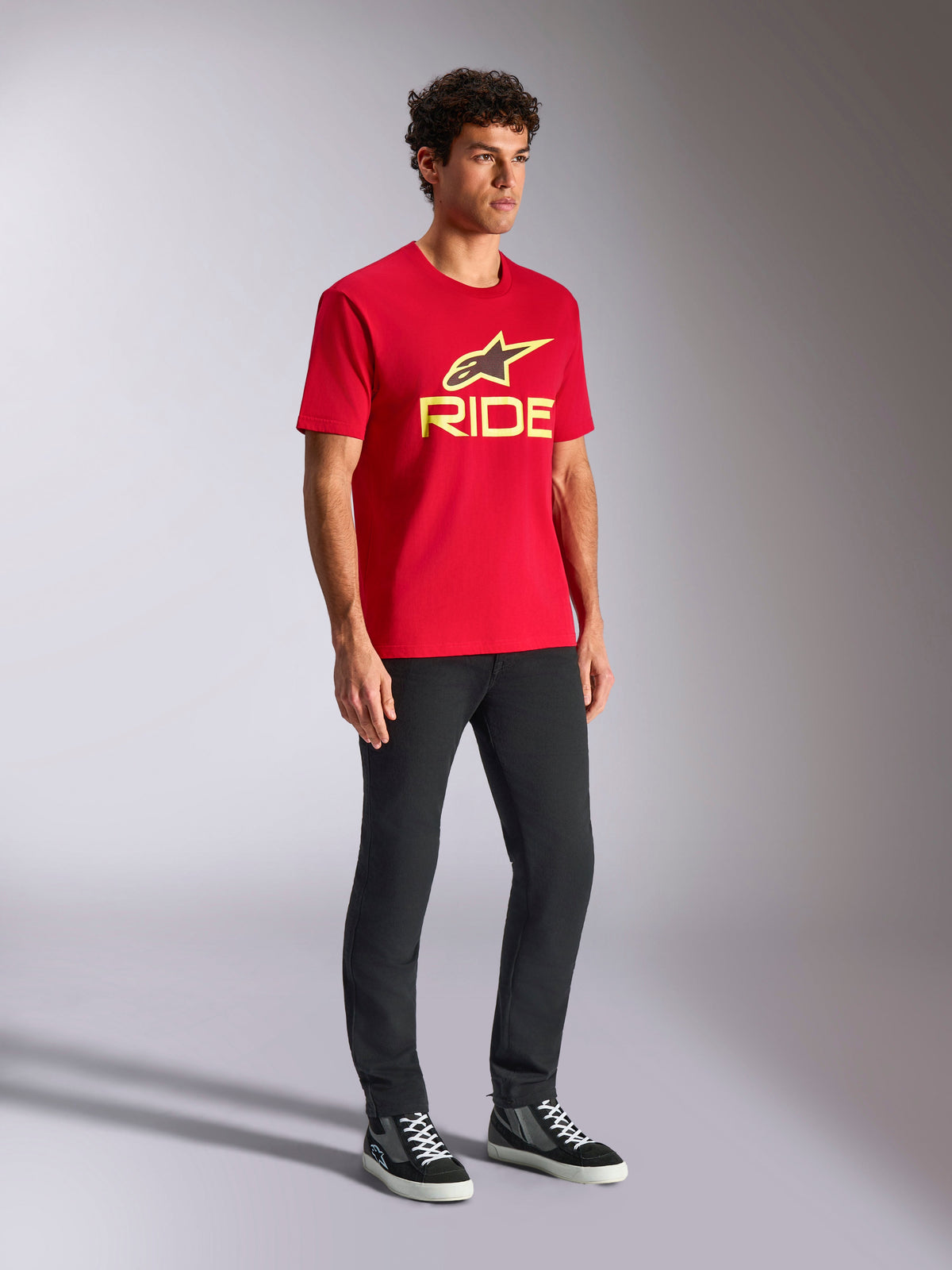 Alpinestars Ride 4.0 CSF Tee, koszulka z krótkim rękawem, czerwona z żółtym i czarnym logo z przodu, zestawiona z czarnymi spodniami i tenisówkami, codzienna odzież uliczna w stylu motorsport