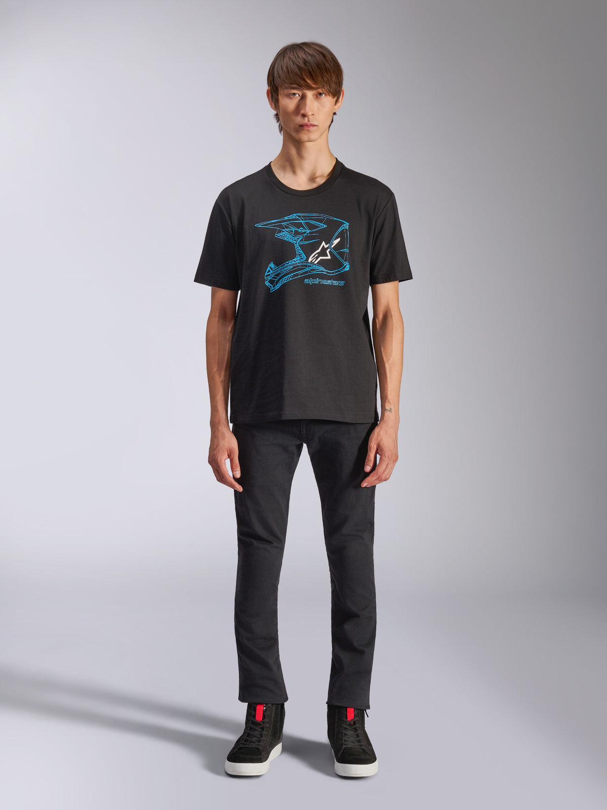 Alpinestars CSF Tee, czarny t-shirt z krótkim rękawem, niebieska grafika z kaskiem motocrossowym i białym logo, model w czarnych spodniach i czarnych sneakersach, casualowy streetwear inspirowany motorsportem