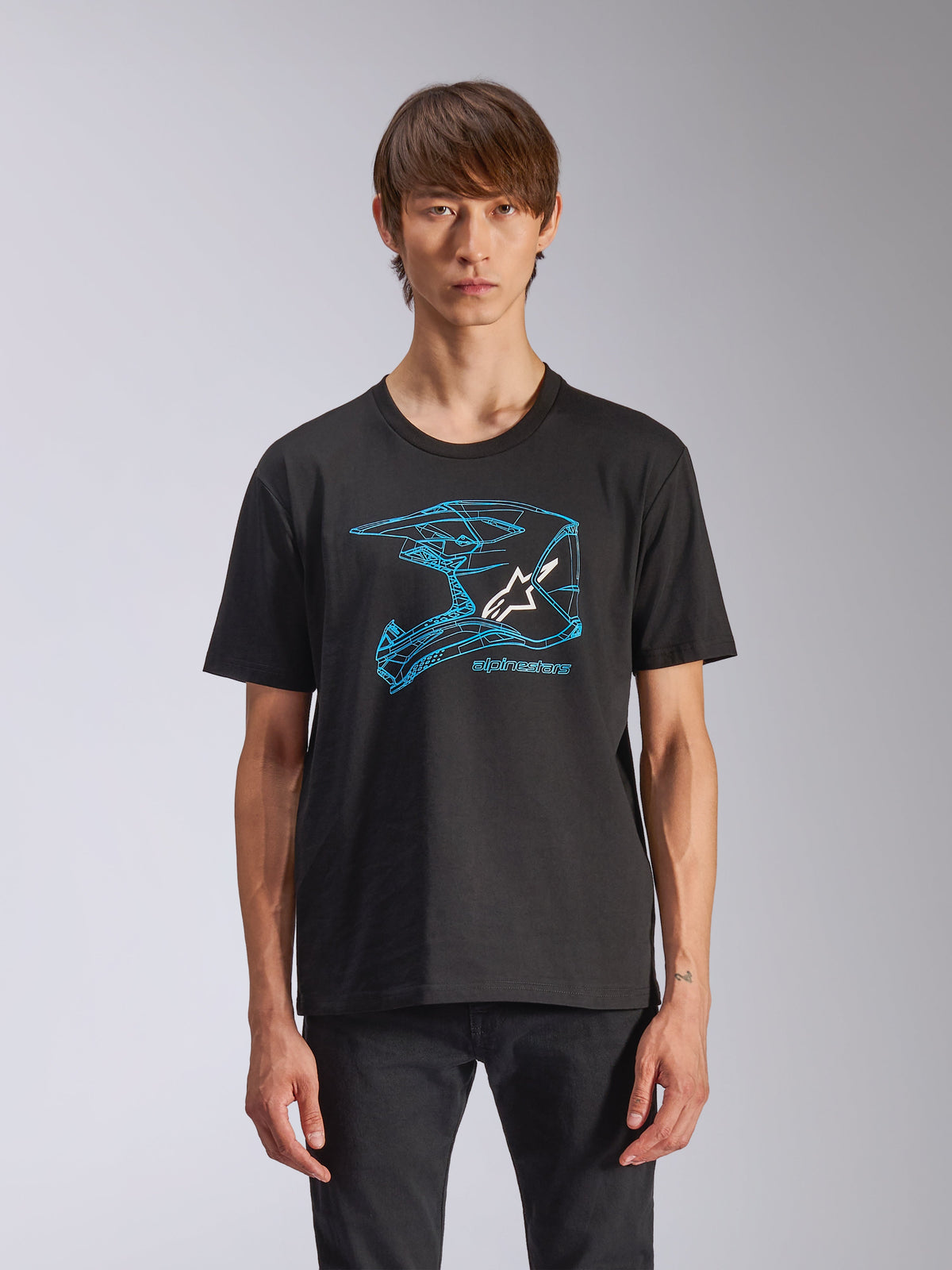 Alpinestars CSF Tee, czarna koszulka z krótkim rękawem, niebieska grafika przedstawiająca kask motocrossowy z białym logo Astars, codzienna odzież uliczna inspirowana sportami motorowymi, prezentowana przez modela