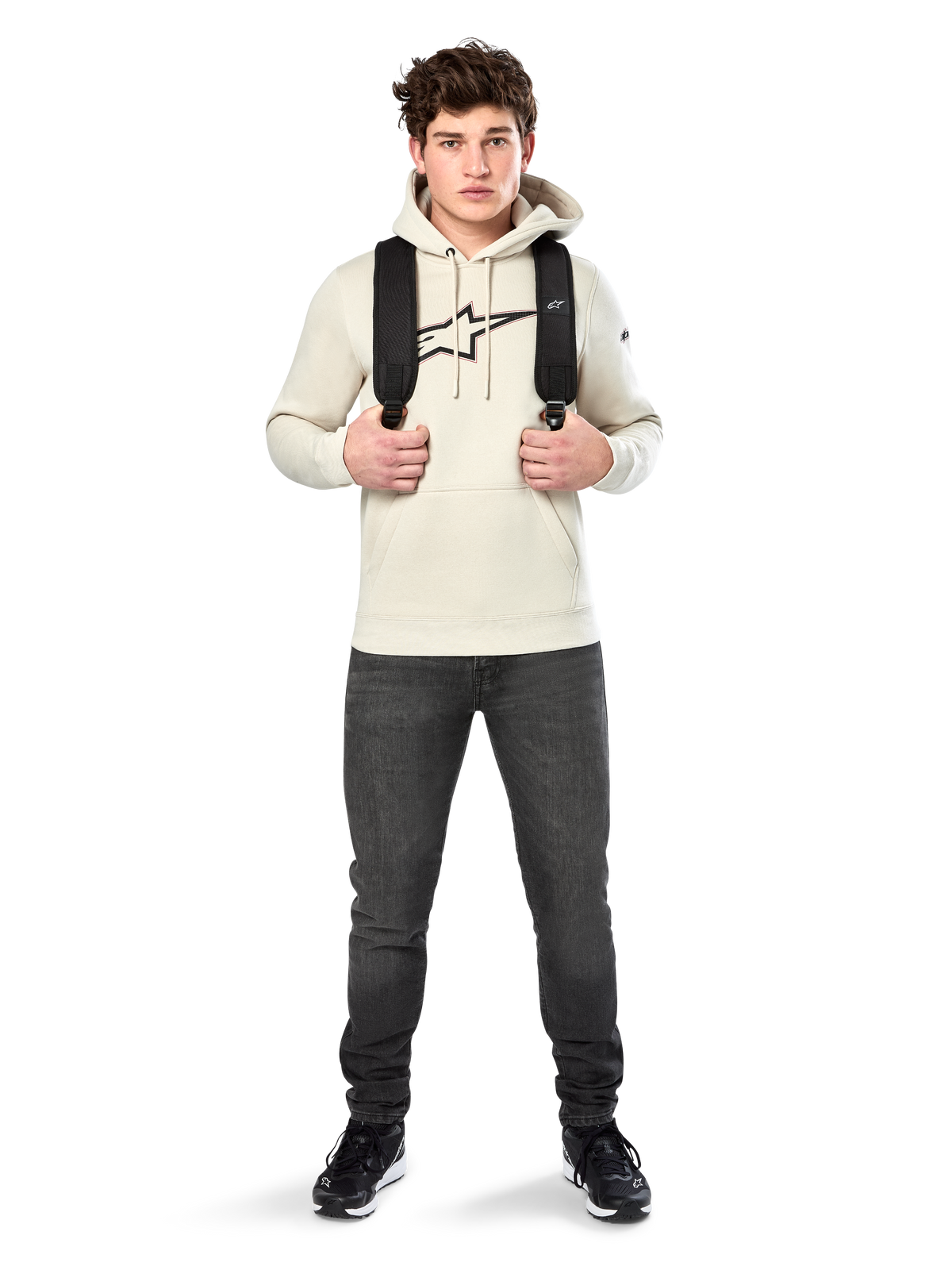 Alpinestars Insignia Hoodie, codzienna odzież streetwear, polarowa bluza w kolorze Off White, logo z motywem włókna węglowego i czerwonym konturem, kaptur ze sznurkiem, kieszeń kangurka, na modelu z czarnym plecakiem i ciemnoszarymi dżinsami