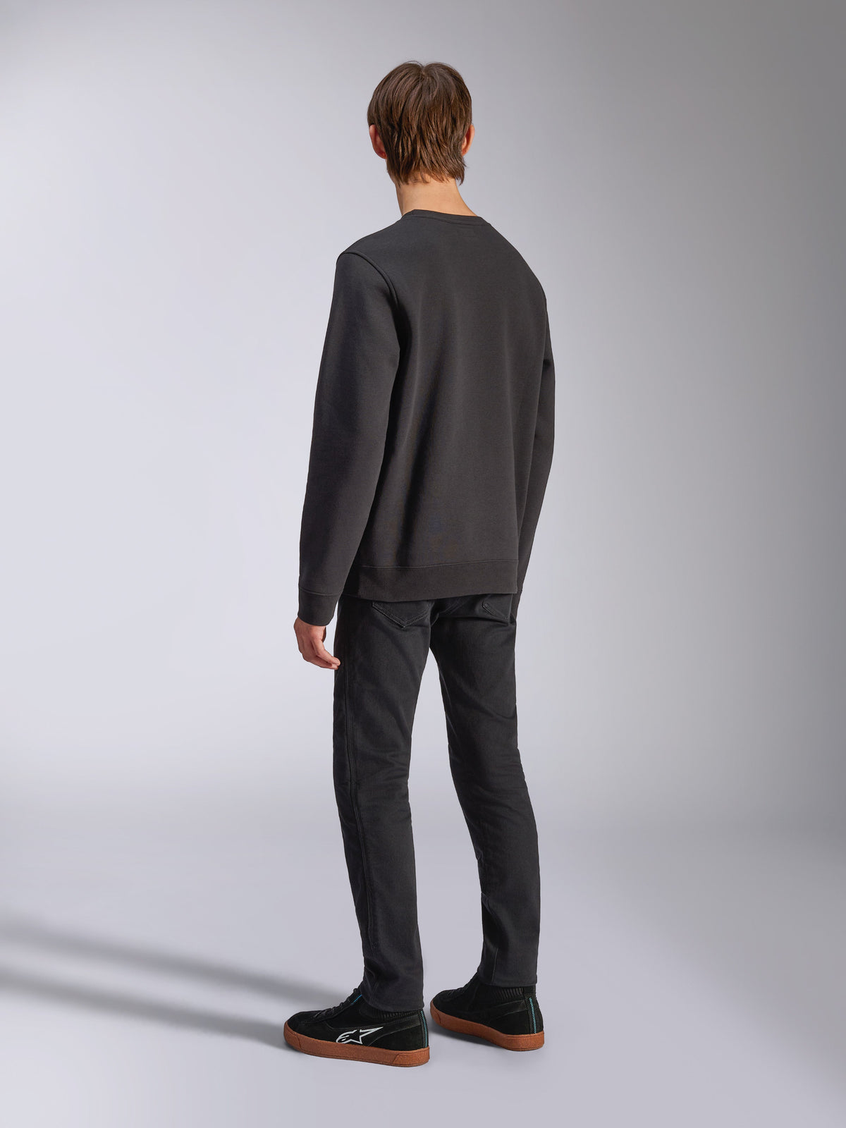 Alpinestars Positive Crew, czarna bluza typu pullover, widok z tyłu na modelu, codzienna odzież streetwearowa inspirowana motorsportem, ze ściągaczami na dole i przy mankietach