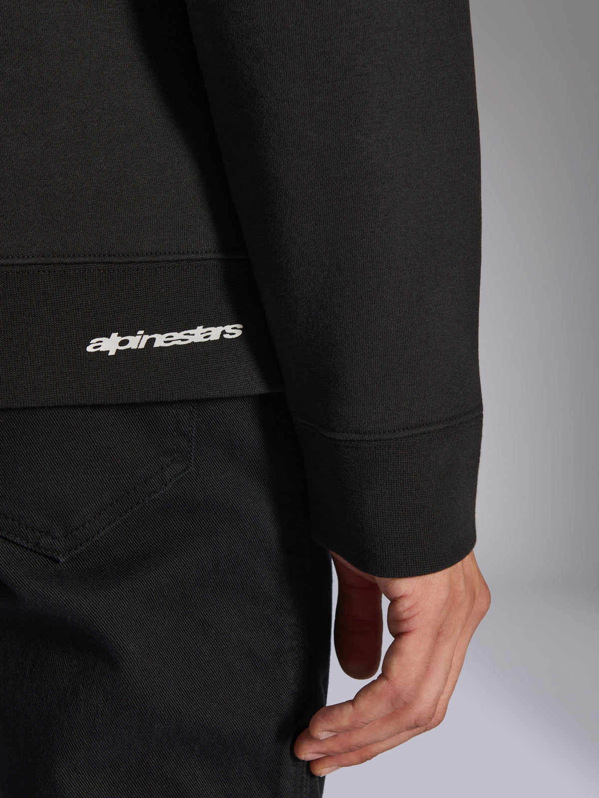Alpinestars Positive Crew, czarna bluza typu pullover, zbliżenie na prążkowany dół i mankiet rękawa z białym logo Alpinestars, tekstura materiału premium, codzienna odzież sportowa inspirowana motorsportem