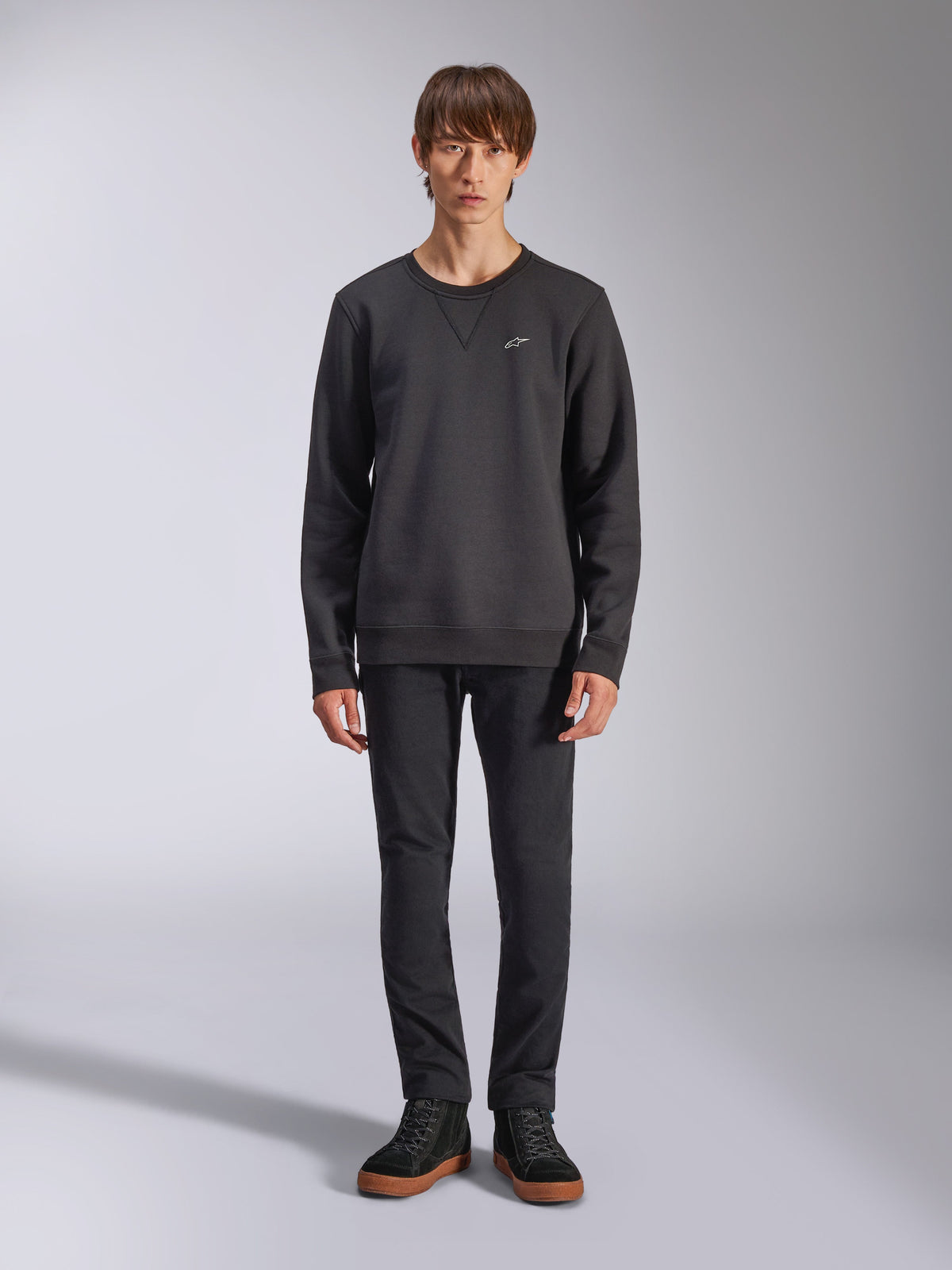Alpinestars Positive Crew Sweatshirt, czarna bluza typu crewneck, małe białe logo na piersi, dekolt z przeszyciem w kształcie litery V, zdjęcie całej sylwetki modela w czarnych spodniach i trampkach, odzież lifestylowa inspirowana sportami motorowymi