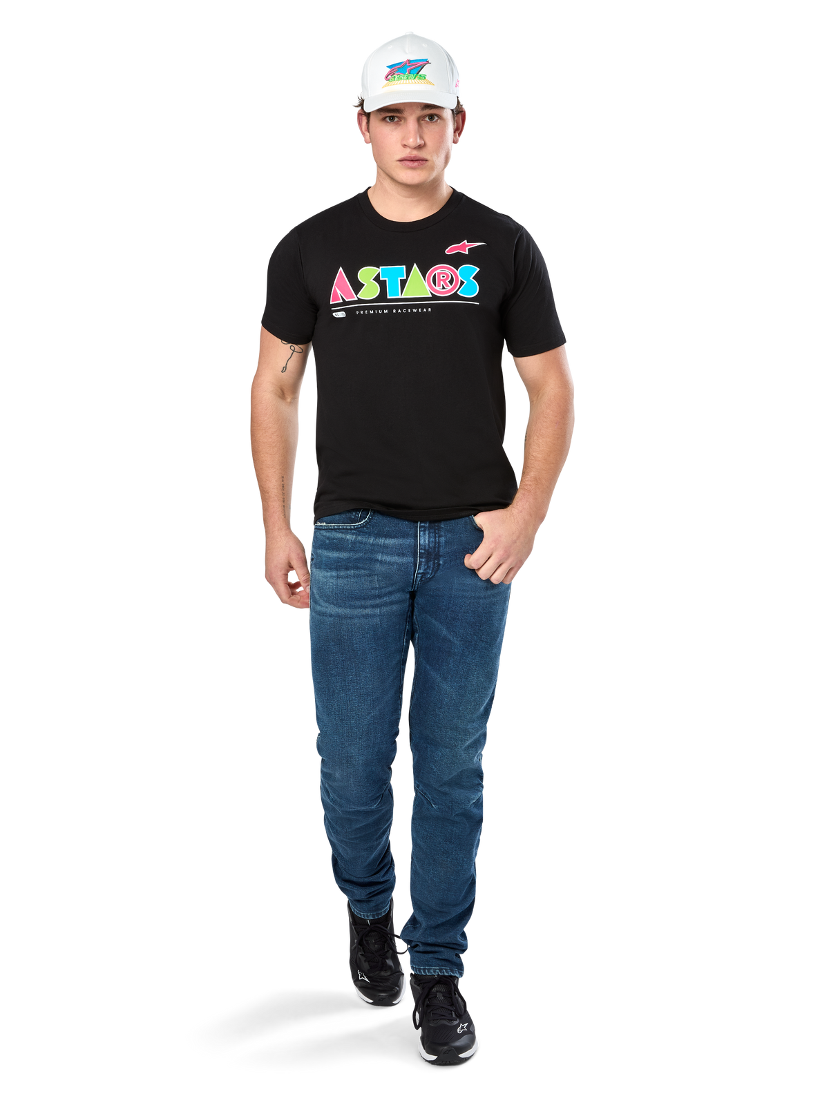 Męski model ubrany w koszulkę Alpinestars Cereal CSF Tee, czarny T-shirt z krótkim rękawem z kolorowym geometrycznym logo ASTARS, zestawiony z niebieskimi jeansami i białą czapką, casualowy styl streetwear inspirowany motorsportem