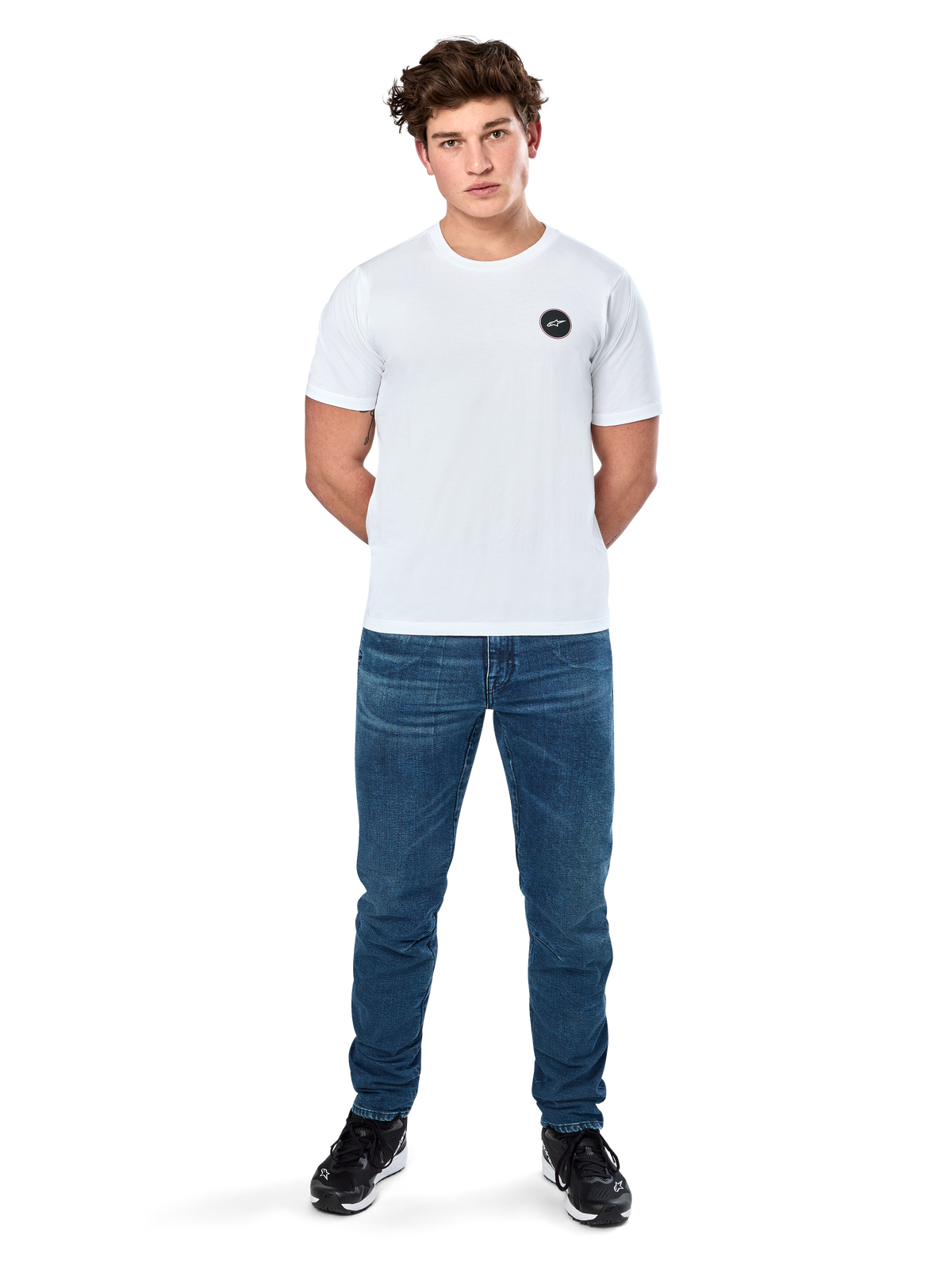 Alpinestars Dot Carbon Csf Tee, koszulka z krótkim rękawem, biała, okrągłe logo Astars o wyglądzie włókna węglowego, codzienna odzież uliczna w stylu motorsport, noszona przez modela w niebieskich jeansach i czarnych sneakersach