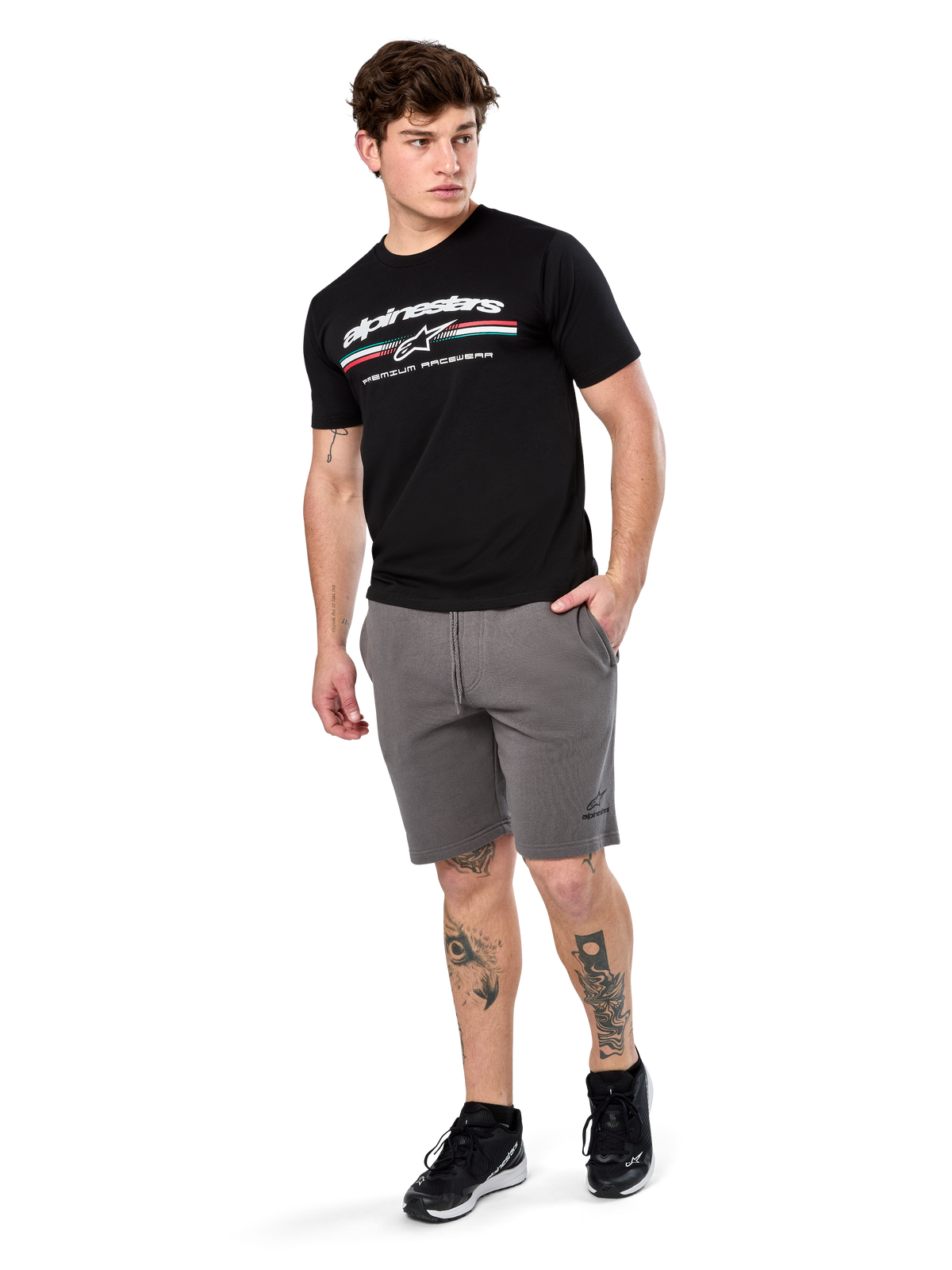 Alpinestars Prevail Csf Tee, koszulka z krótkim rękawem, czarna, białe logo Alpinestars z trójkolorowym paskiem w stylu paddock, noszona z szarymi szortami i czarnymi sneakersami, codzienna odzież streetwearowa w stylu motorsportowym