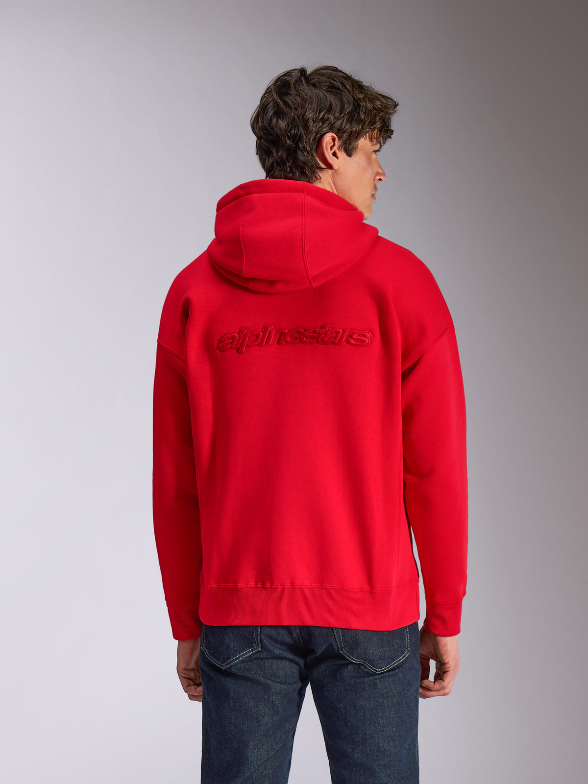 Alpinestars Emergent Oversized Hoodie, czerwona, widok z tyłu na modelu, haftowane wypukłe logo Alpinestars ton w ton, luźny krój ze ściągaczami na dole i przy mankietach, codzienny streetwear inspirowany motorsportem