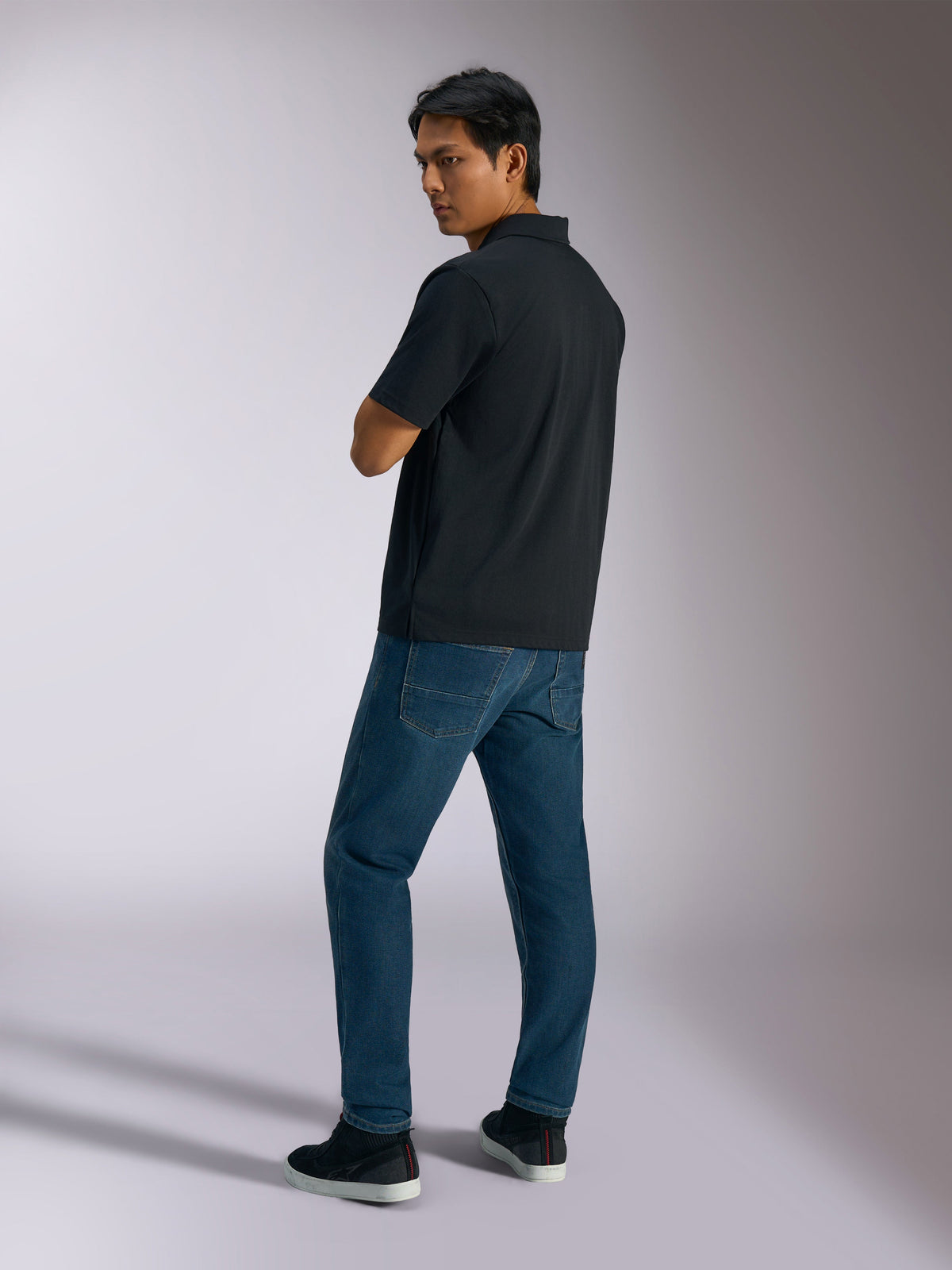 Alpinestars Impetus Sport Polo, Black, short-sleeve polo shirt with mock mesh texture and three-button placket, worn by a model with blue jeans and black sneakers, casual motorsport-inspired streetwear