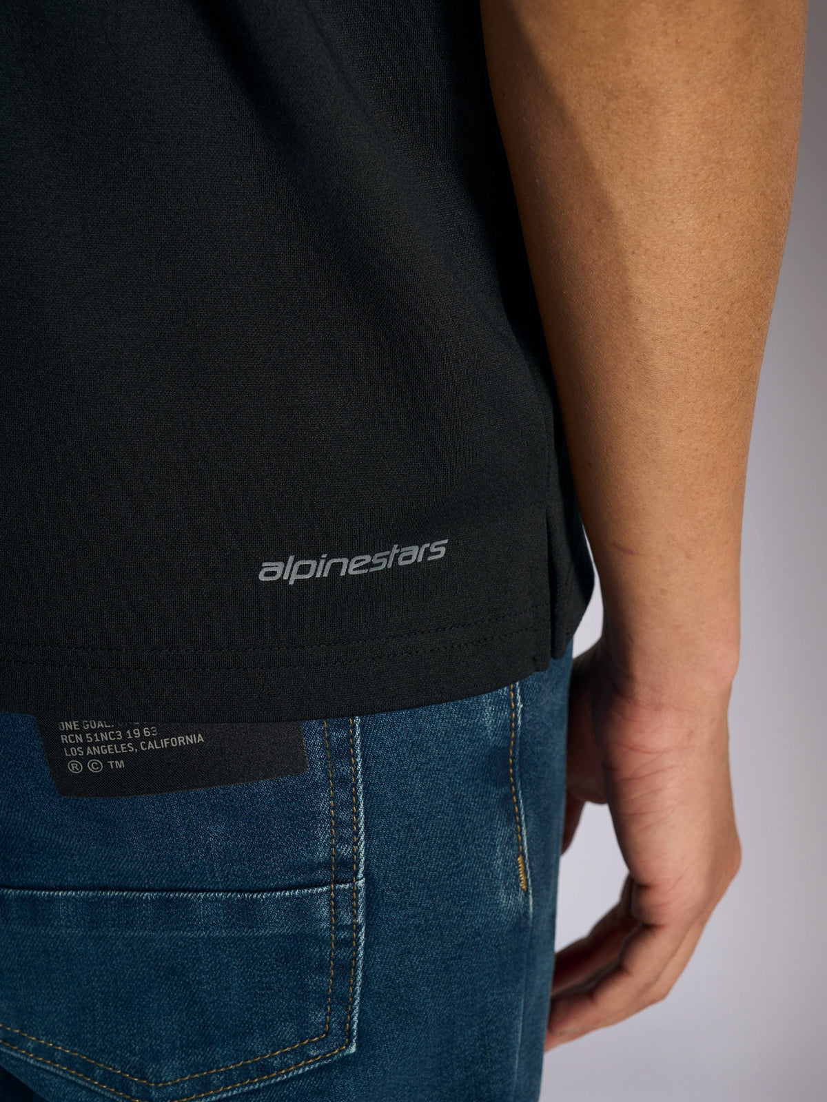 Alpinestars Impetus Sport Polo, detail view of the bottom hem and side vent, Black with grey Alpinestars wordmark branding, casual motorsport-inspired sportswear