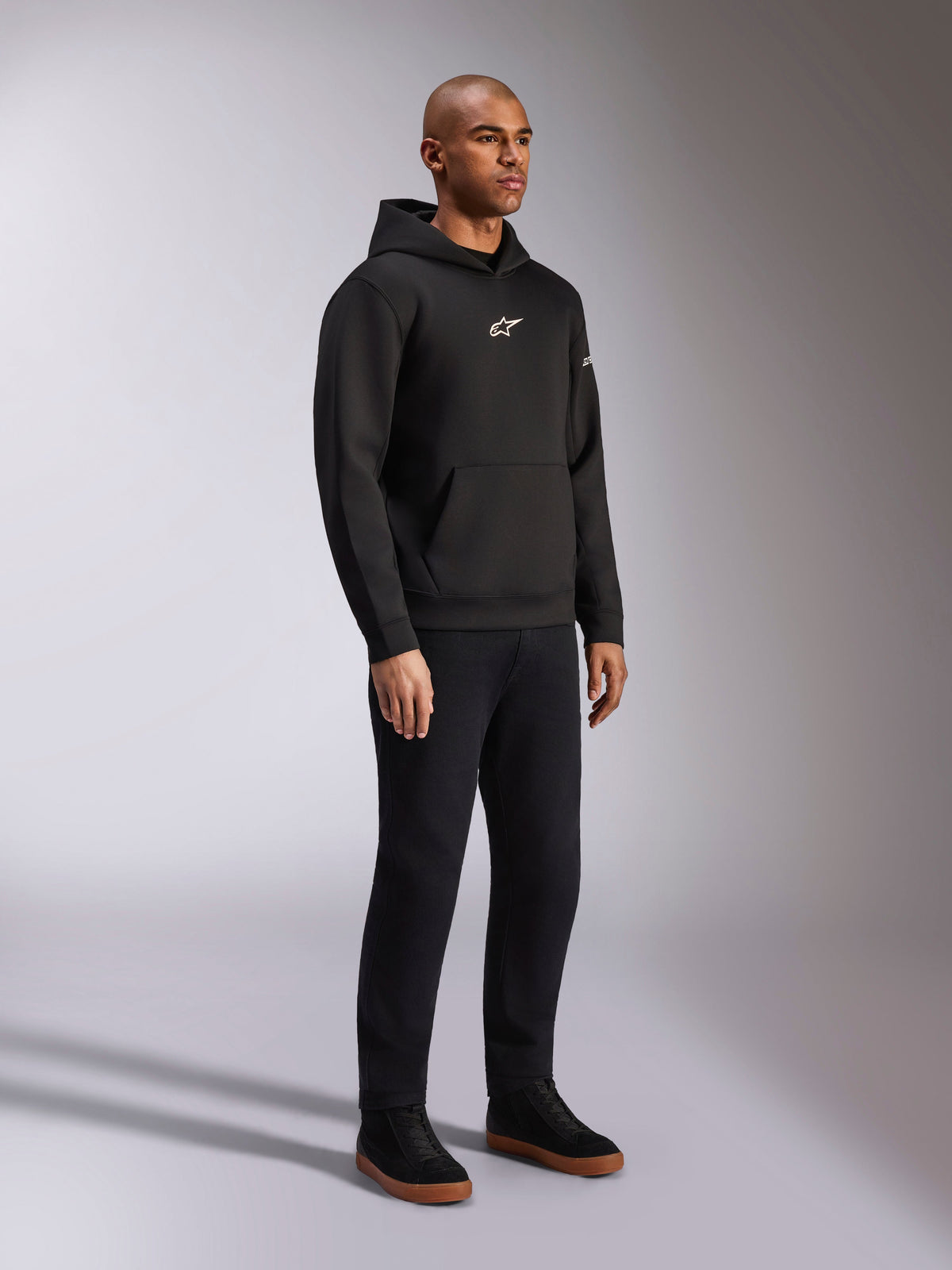 Alpinestars Insight Hoodie, Black, casual pull-over fleece hoodie with white Astars logo on the chest, kangaroo pocket, worn with black pants and sneakers, full-body studio shot, motorsport-inspired streetwear