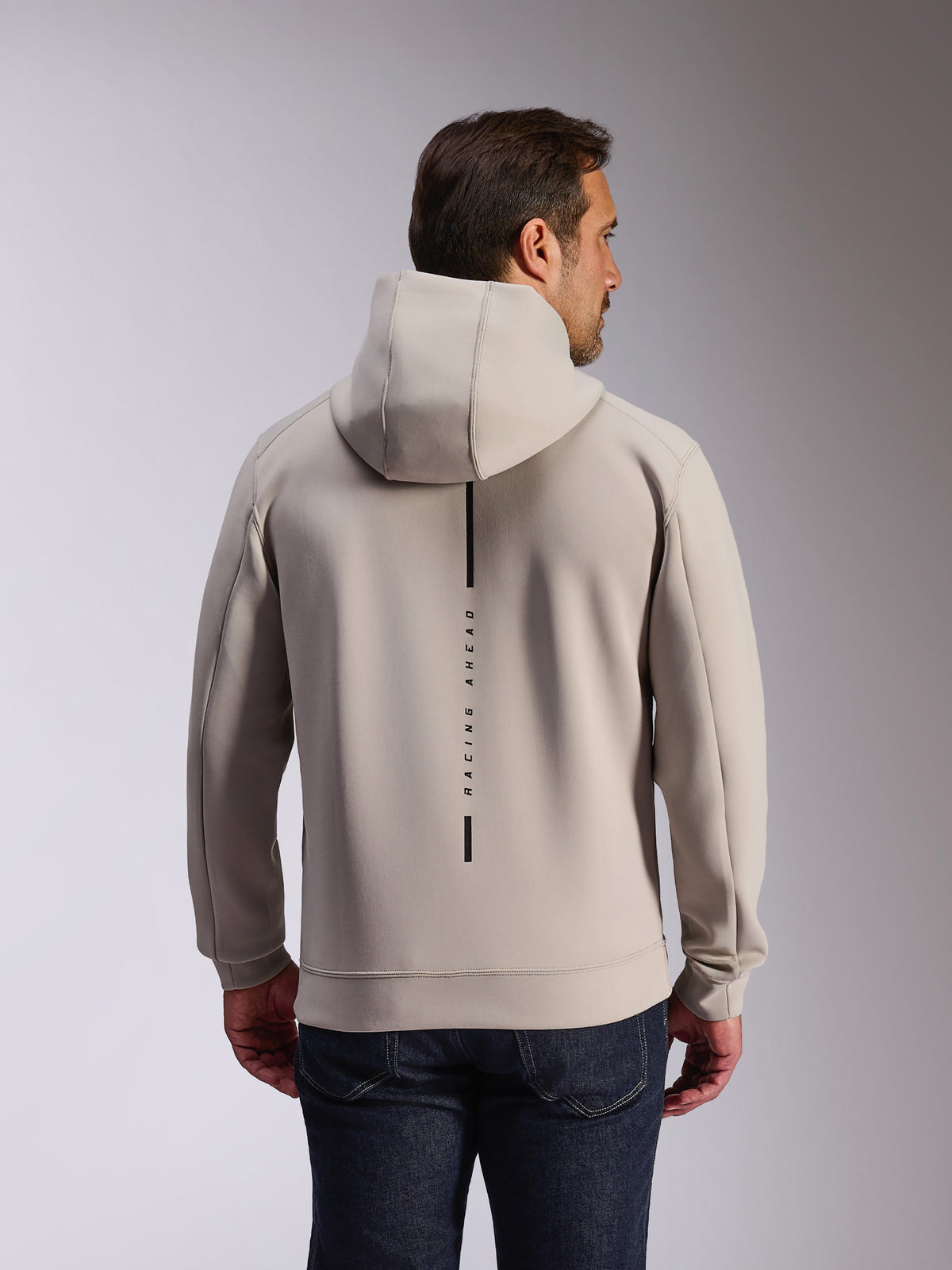 Alpinestars Insight Hoodie w kolorze Cement, widok z tyłu modelu w jasnoszarej bluzie z kapturem, czarny pionowy logotyp z napisem „RACING AHEAD”, codzienna bluza z dwuwarstwowego polaru inspirowana motorsportem