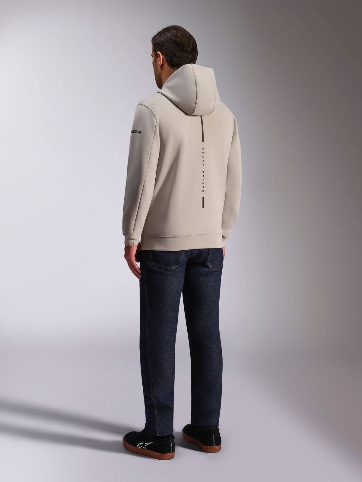 Alpinestars Insight Hoodie, widok z tyłu w kolorze cement gray, z pionowym czarnym pasem i napisem "RACING AHEAD", casualowy design streetwear, zestawiona z ciemnymi dżinsami i czarnymi butami