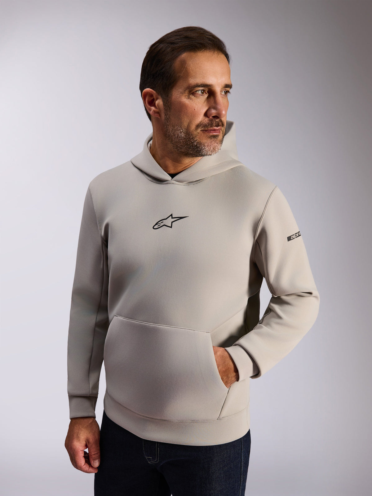 Alpinestars Insight Hoodie, szara bluza z kapturem typu lifestyle, polar w kolorze Cement, czarne logo Astars na piersi, kieszeń kangurka, napis na rękawie, nowoczesny design inspirowany motorsportem