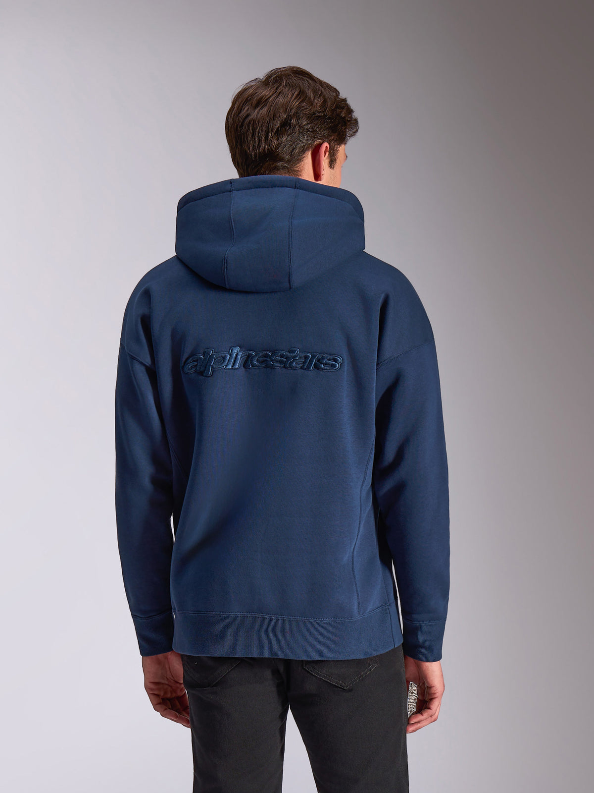 Alpinestars Emergent Oversized Hoodie, granatowa bluza z kapturem, widok z tyłu z tonalnym haftowanym logo Alpinestars, luźny krój oversize, kaptur ze sznurkiem i ściągacze przy mankietach, streetwear inspirowany motorsportem