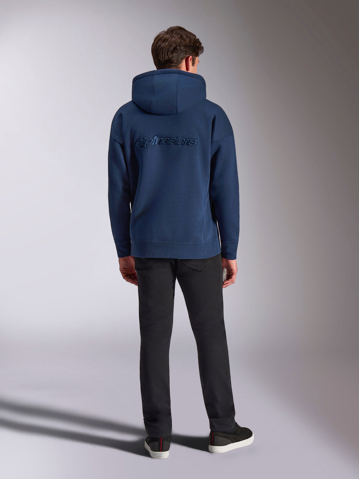 Alpinestars Emergent Oversized Hoodie, granatowa bluza z kapturem, codzienny styl streetwearowy, wyszywany napis Alpinestars w tym samym odcieniu na plecach, luźny krój, w połączeniu z czarnymi spodniami, widok z tyłu