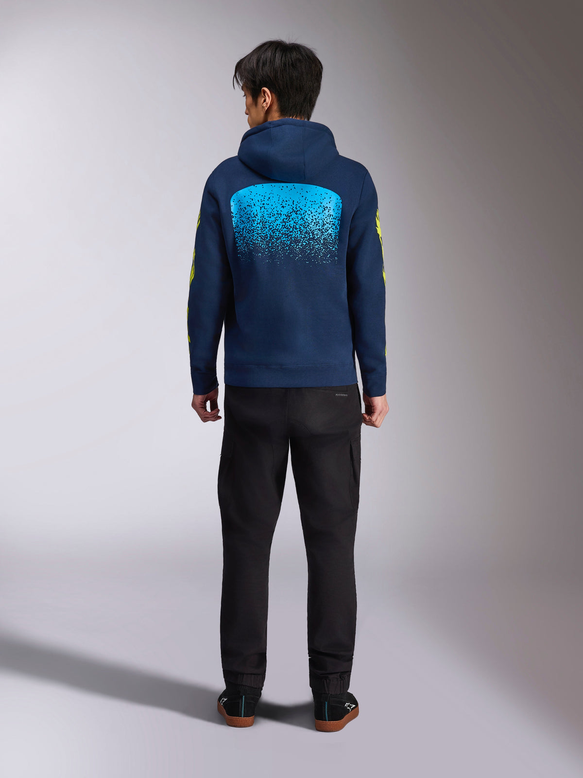 Alpinestars Obsessed Hoodie, granatowa bluza z kapturem, widok z tyłu, duża cyjanowa grafika MX z gradacją, żółte logo na rękawach, codzienna bluza polarowa inspirowana sportami motorowymi