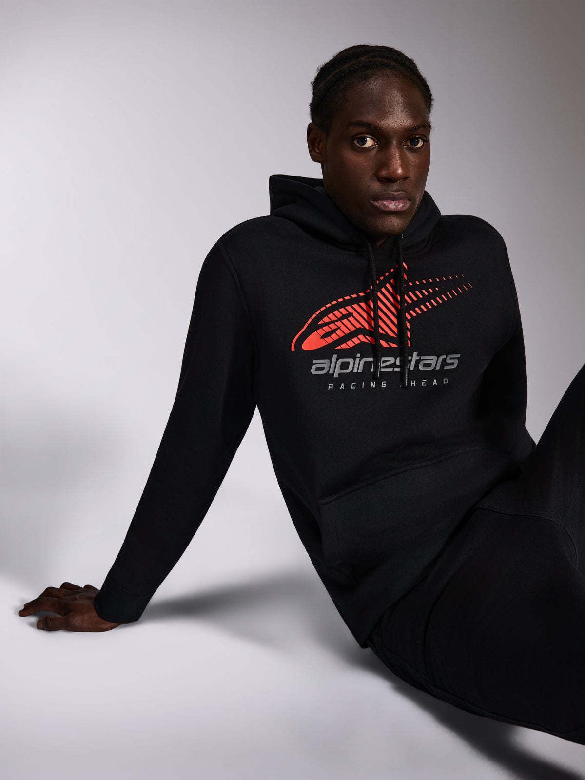 Alpinestars Pulse Hoodie, Black, casual streetwear worn by model, featuring red speed line fade Astars logo and 'alpinestars RACING AHEAD' text on chest, drawstring hood, long sleeves, modern motorsport-inspired design