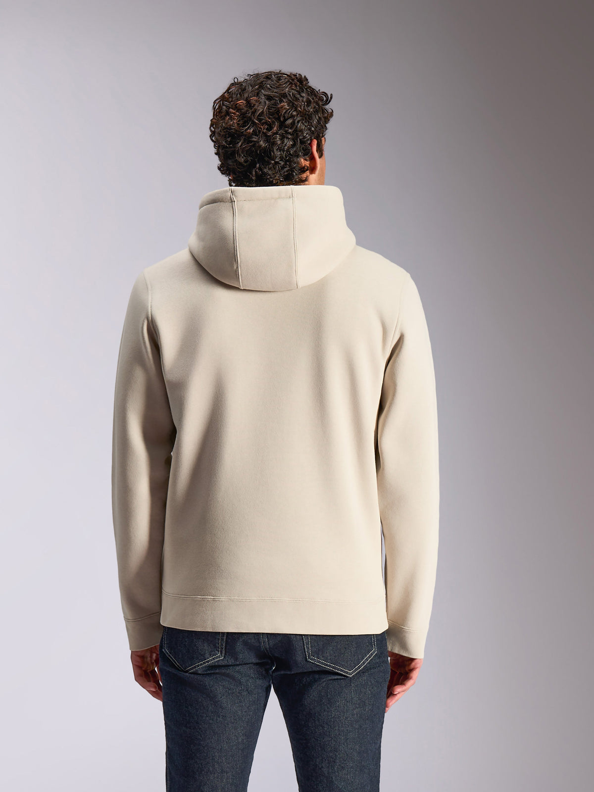 Alpinestars Pulse Hoodie, kolor piaskowy, widok z tyłu na modela ubranego w gładką bluzę z kapturem, zestawiona z ciemnymi jeansami, casualowy streetwear inspirowany sportami motorowymi