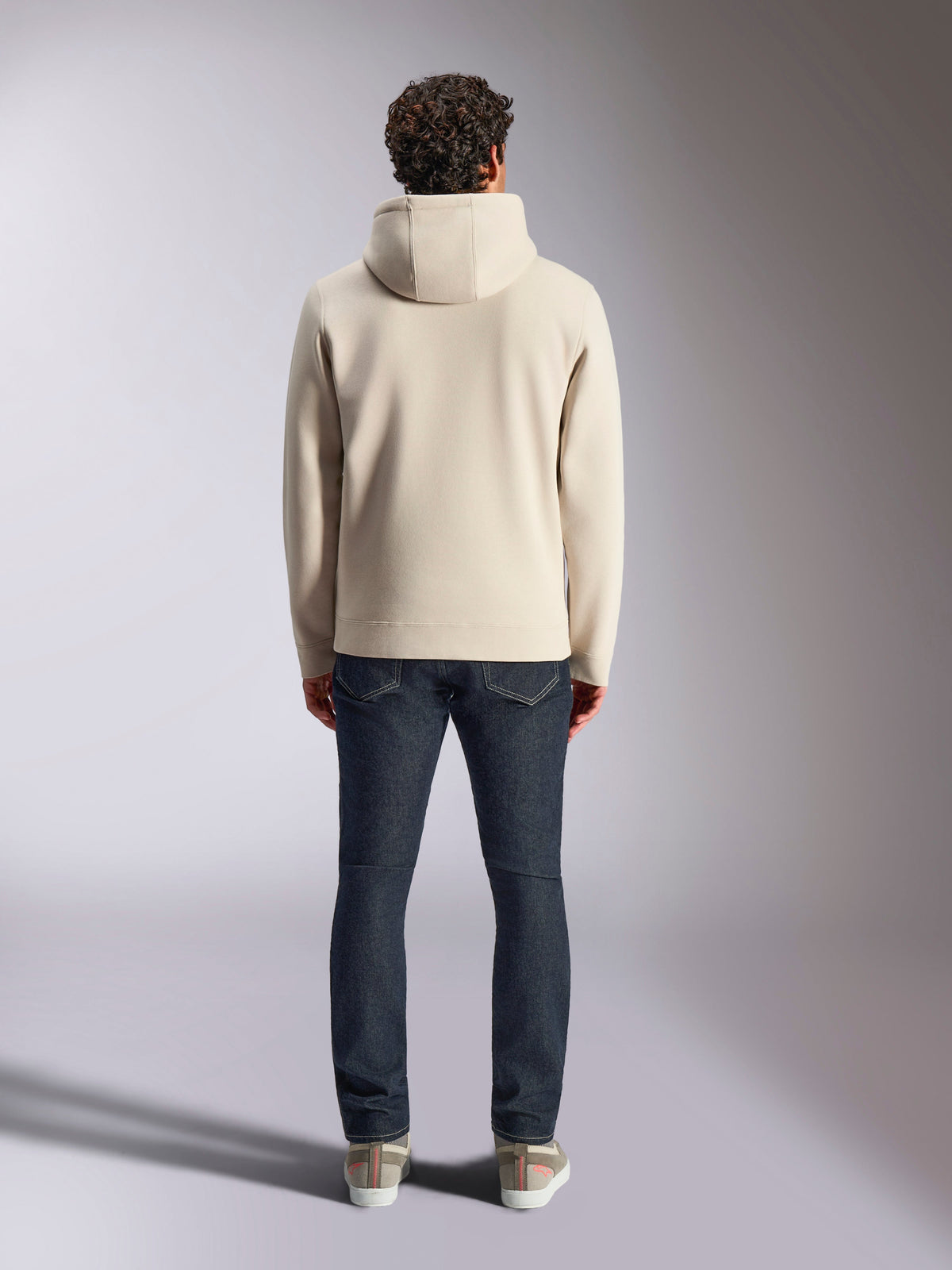 Alpinestars Pulse Hoodie, codzienna odzież streetwearowa, Off White, widok z tyłu na modelu w ciemnych jeansach i sneakersach, polarowa bluza z kapturem ze ściągaczami przy mankietach i na dole