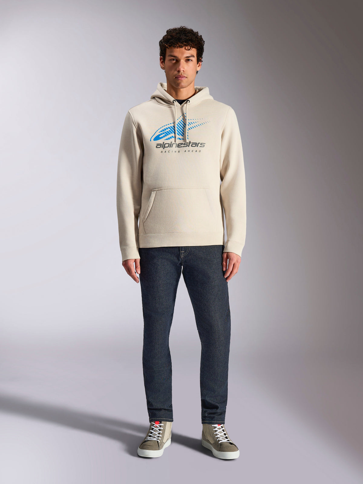 Alpinestars Pulse Hoodie, kolor off-white, bluza z kapturem typu pullover, niebiesko-czarne logo Astars Combo z efektem speed line fade, stylizacja z ciemnymi dżinsami i sneakersami, casualowy streetwear w stylu motorsport