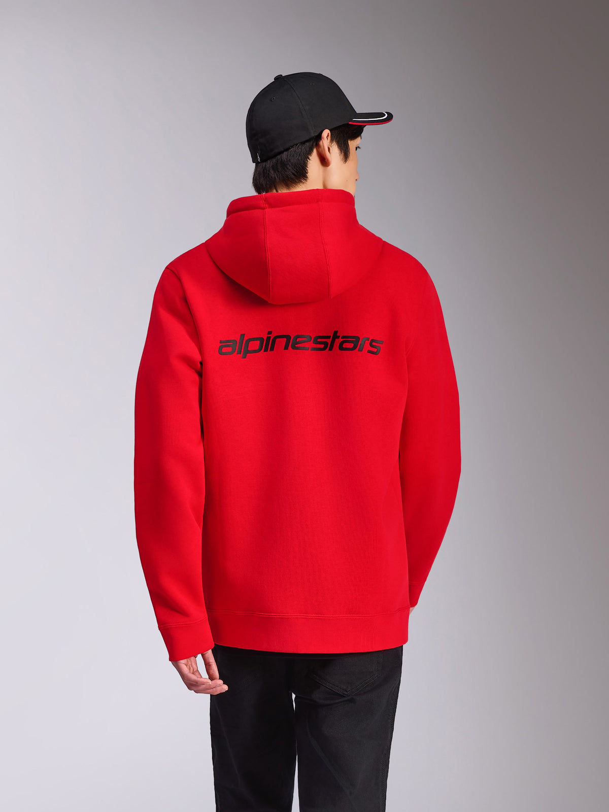 Alpinestars Transverse Hoodie, czerwona, widok z tyłu z czarnym napisem Alpinestars na plecach, codzienna odzież streetwear, polarowa bluza z kapturem ze ściągaczami przy mankietach i u dołu, stylizacja z czarną czapką