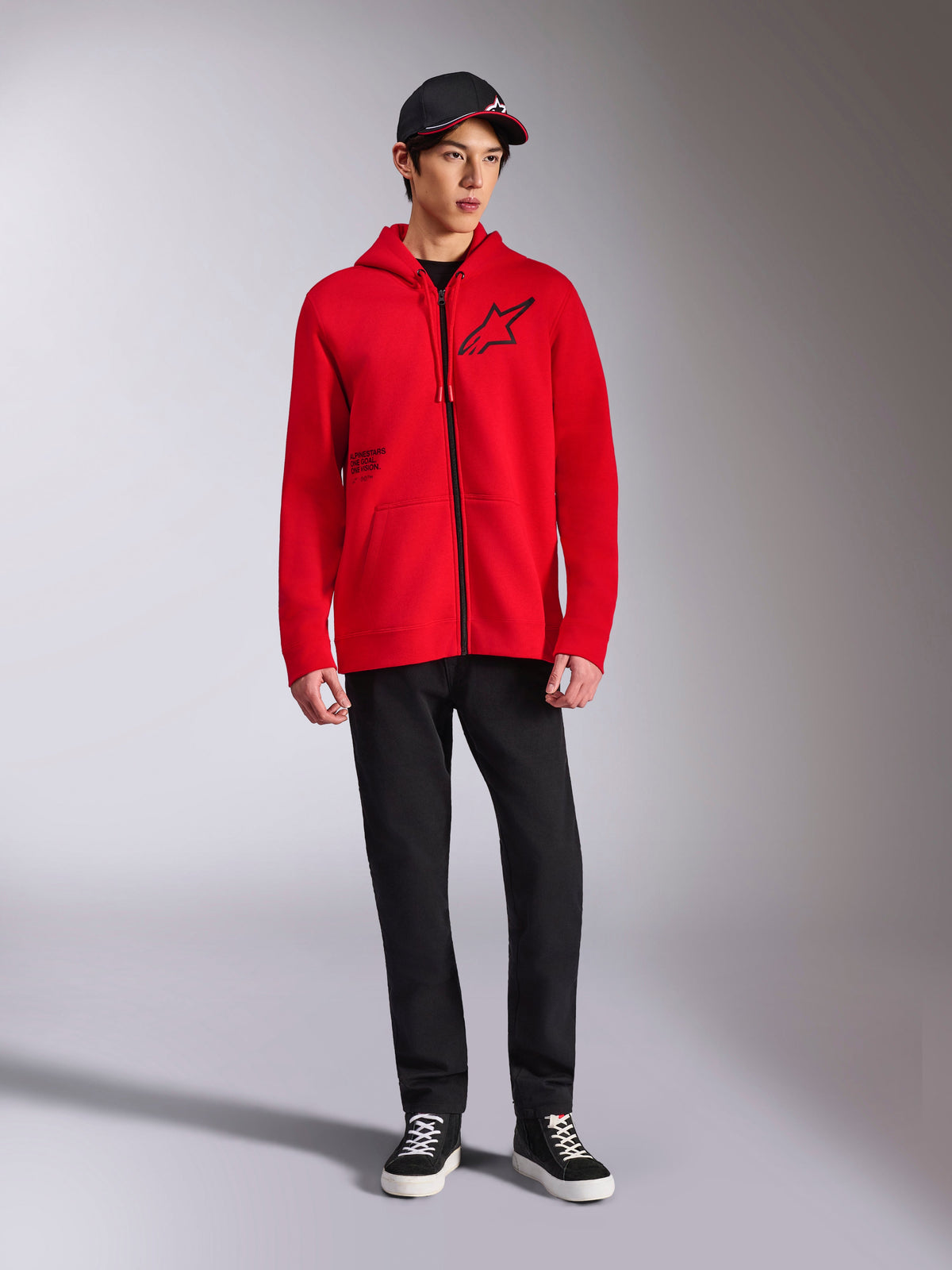 Alpinestars Transverse Hoodie, czerwona bluza polarowa zapinana na pełny zamek, czarne logo Astars na piersi i nadruk One Goal z boku, noszona przez modela z czarnymi spodniami i czapką, casualowy streetwear inspirowany sportami motorowymi