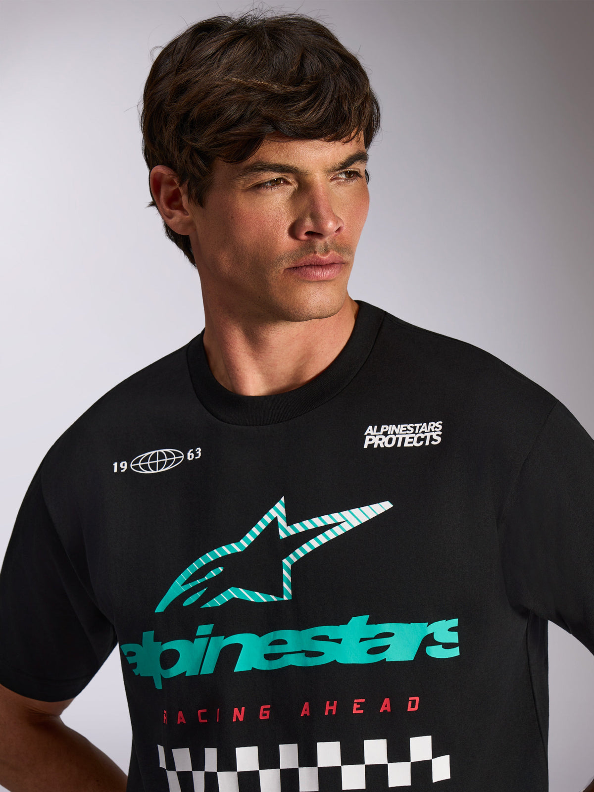 Alpinestars Aplomb Oversized CSF Tee, Short Sleeve T-Shirt, Black, teal and white Astars combo logo with 'Racing Ahead' text and checkered pattern, worn by a male model, casual motorsport streetwear
