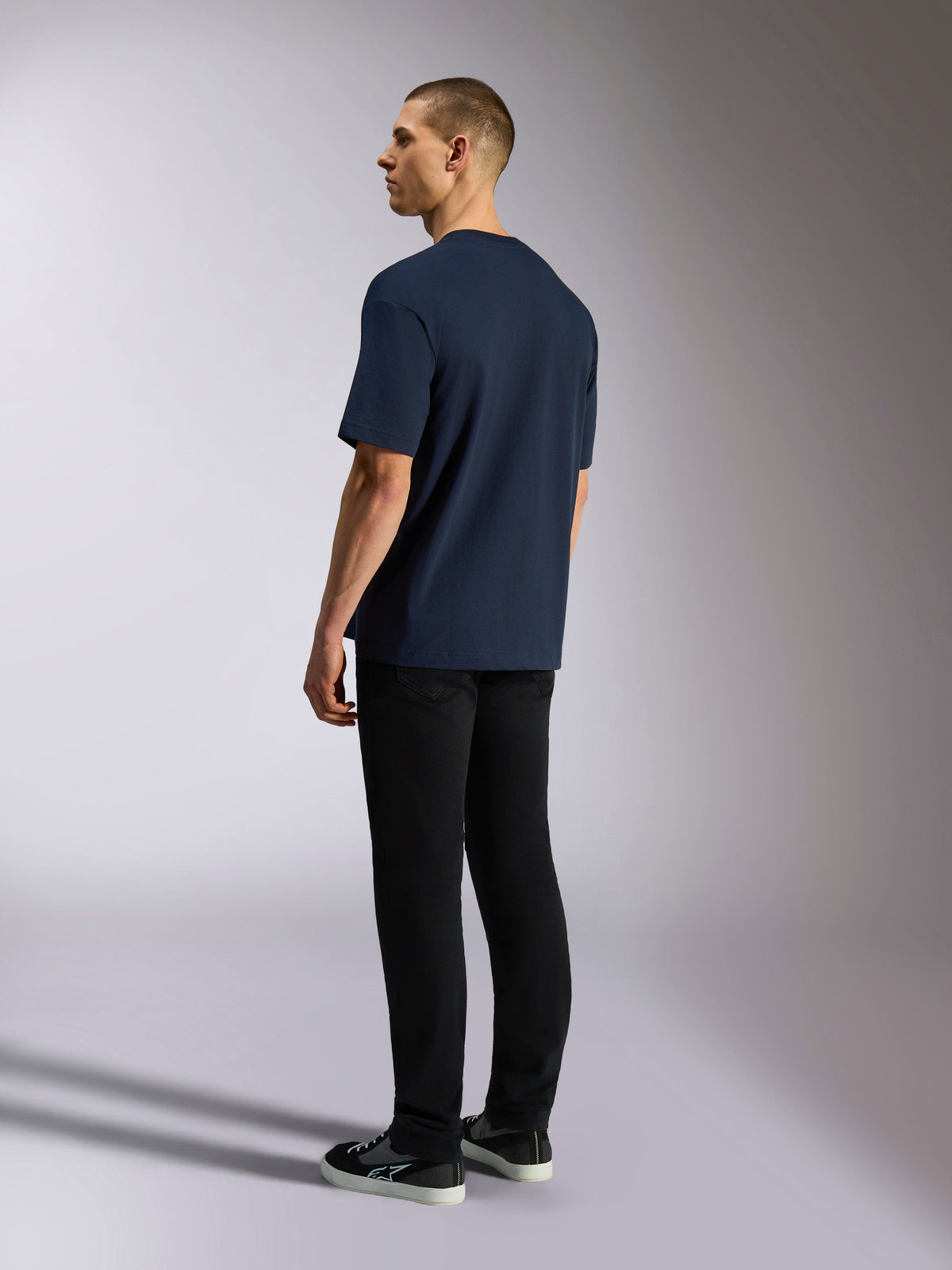 Alpinestars Aplomb Oversized CSF Tee, koszulka z krótkim rękawem, granatowa, widok z tyłu na modelu, zestawiona z czarnymi spodniami i sneakersami, casualowy streetwear inspirowany sportami motorowymi
