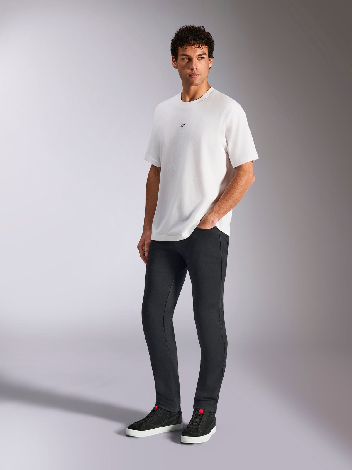Alpinestars Focused Oversized CSF Tee, Short Sleeve T-Shirt, White, featuring a small black Astars chest logo, worn by male model with dark pants and black sneakers, casual motorsport-inspired streetwear