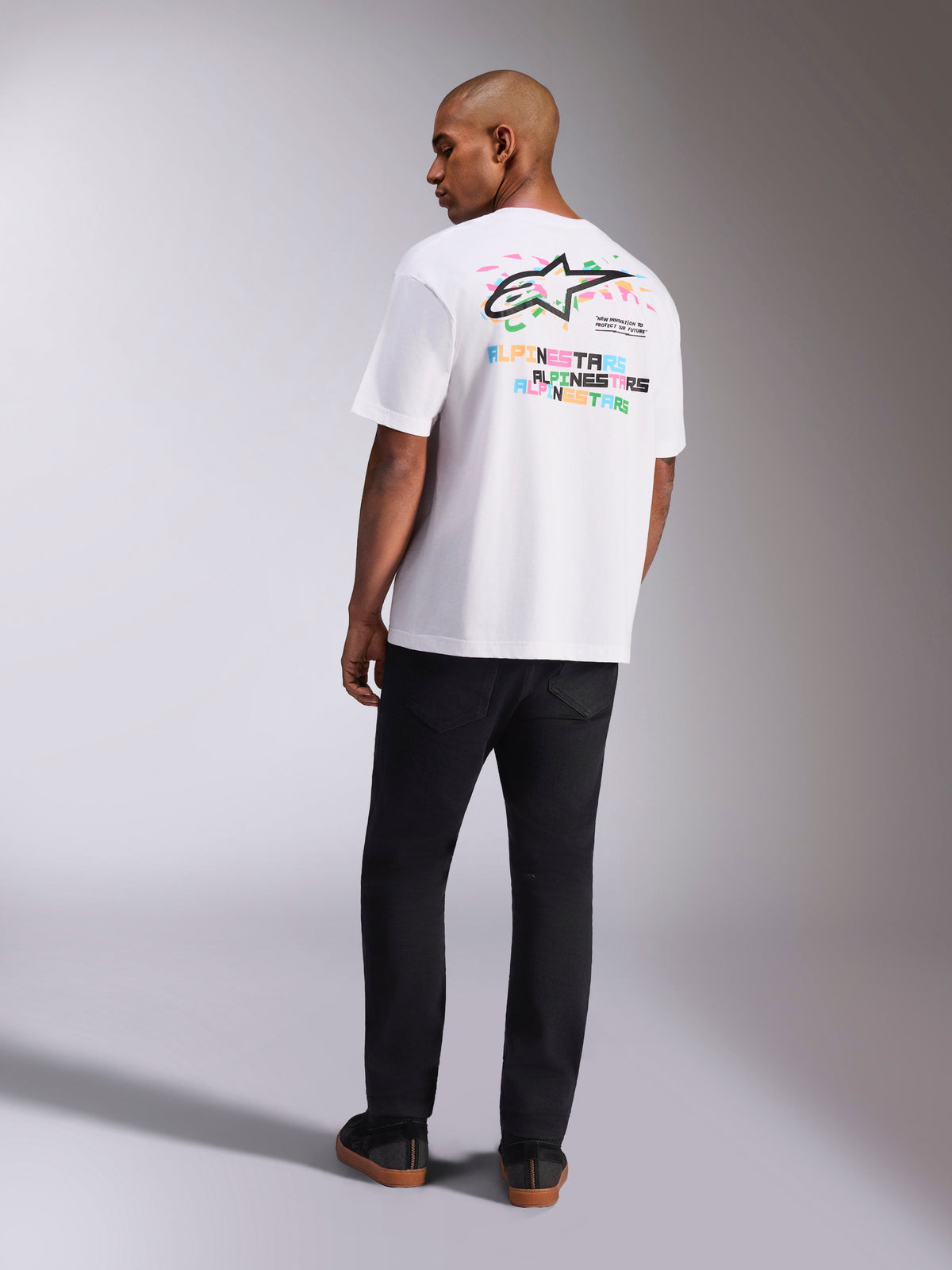 Alpinestars Wild Oversized CSF Tee, Short Sleeve T-Shirt, White, Rear view of model wearing oversized tee with vibrant multi-color Astars logo and stacked text on the back, casual motorsport-inspired streetwear