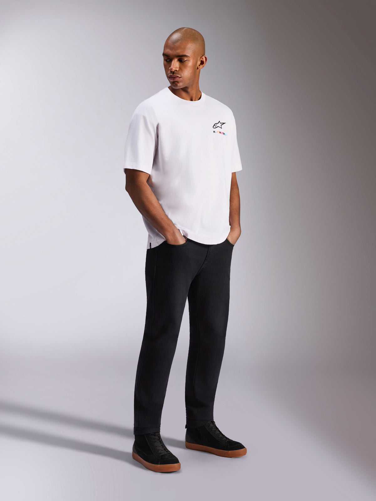Alpinestars Wild Oversized CSF Tee, Short Sleeve T-Shirt, White, featuring a small multicolor Astars logo on the chest, worn by a model with black pants and black sneakers, casual motorsport-inspired streetwear