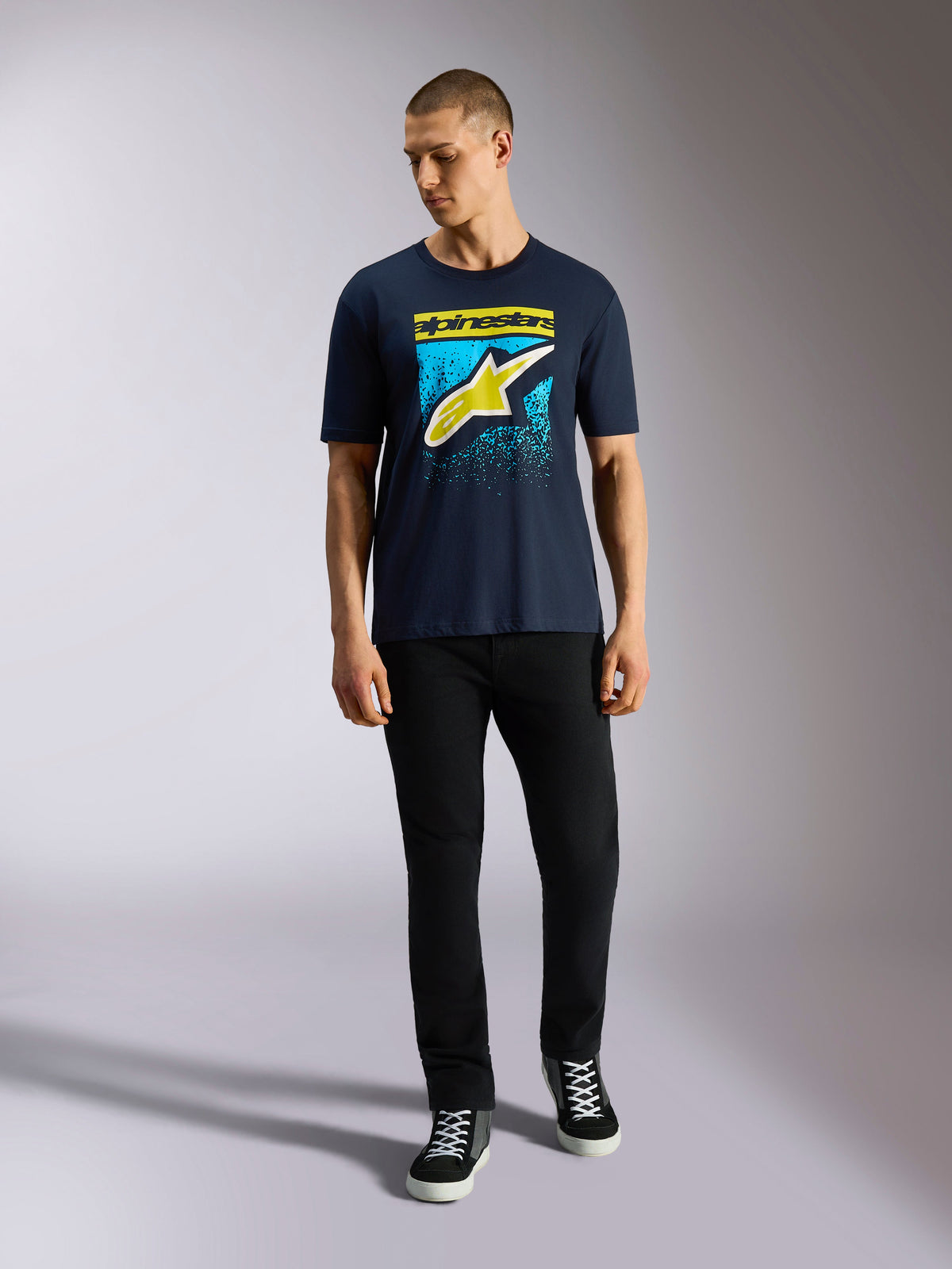 Alpinestars Noka CSF Tee, koszulka z krótkim rękawem, granatowa, logo Astars z przodu z żółtą i jasnoniebieską gradacją MX, prezentowana przez modela w czarnych spodniach, casualowa odzież motorsportowa streetwear