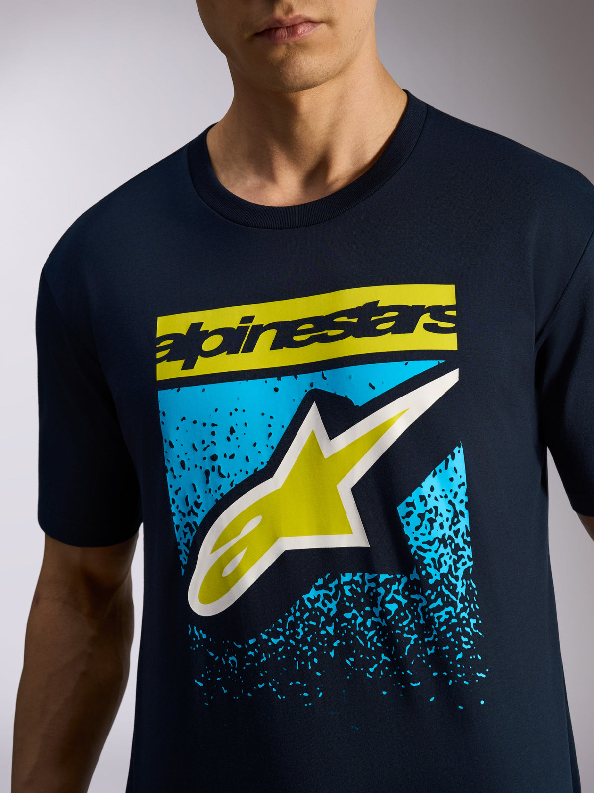Alpinestars Noka CSF Tee, granatowa koszulka z krótkim rękawem, żółty napis Alpinestars i logo z gwiazdą na tle niebieskiej grafiki z gradacją MX, sportowa odzież codzienna