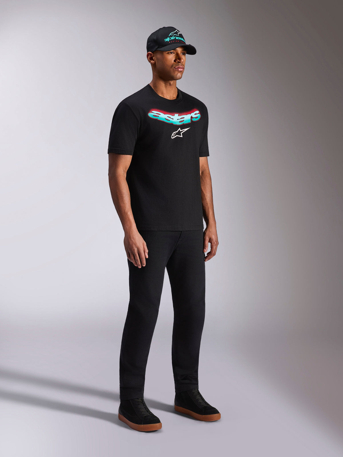 Alpinestars Ellipsoid CSF Tee, czarna koszulka z krótkim rękawem, turkusowo-czerwony gradientowy nadruk Astars z białym logo, męski model w codziennym stroju streetwearowym z czarną czapką i spodniami