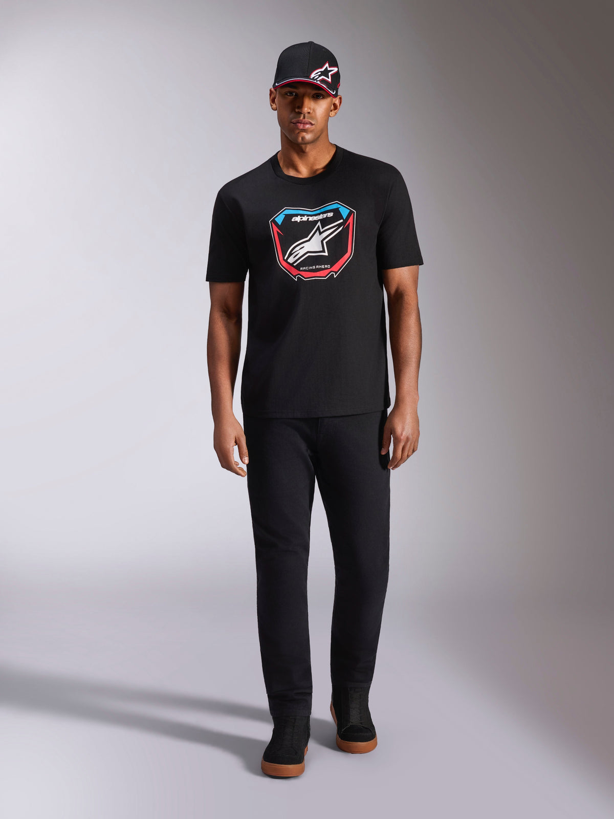 Alpinestars Plate CSF Tee, Short Sleeve T-Shirt, Black, Front MX plate graphic with white Astars logo and blue and red accents, worn by model with matching black cap and pants, casual motorsport sportswear