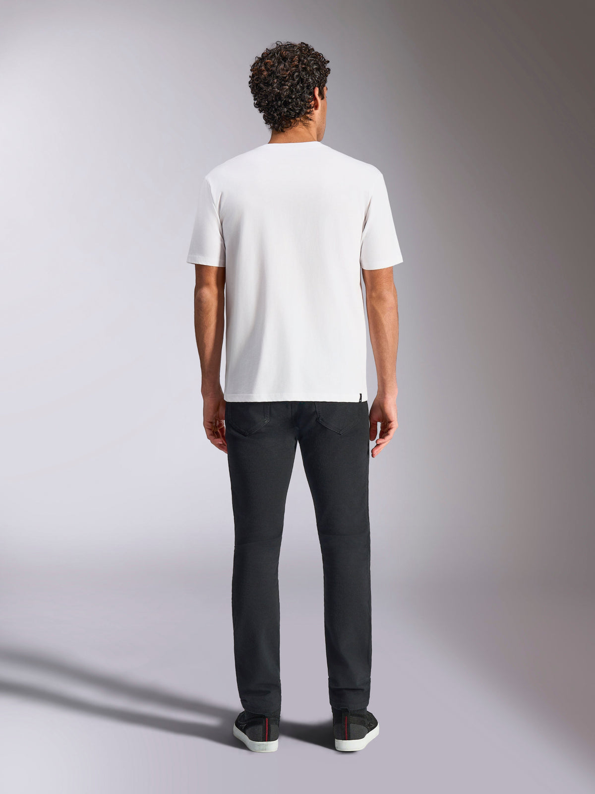 Alpinestars Plate CSF Tee, biała koszulka z krótkim rękawem, widok z tyłu na modelu, w zestawieniu z czarnymi spodniami, casualowa odzież uliczna w stylu motorsport