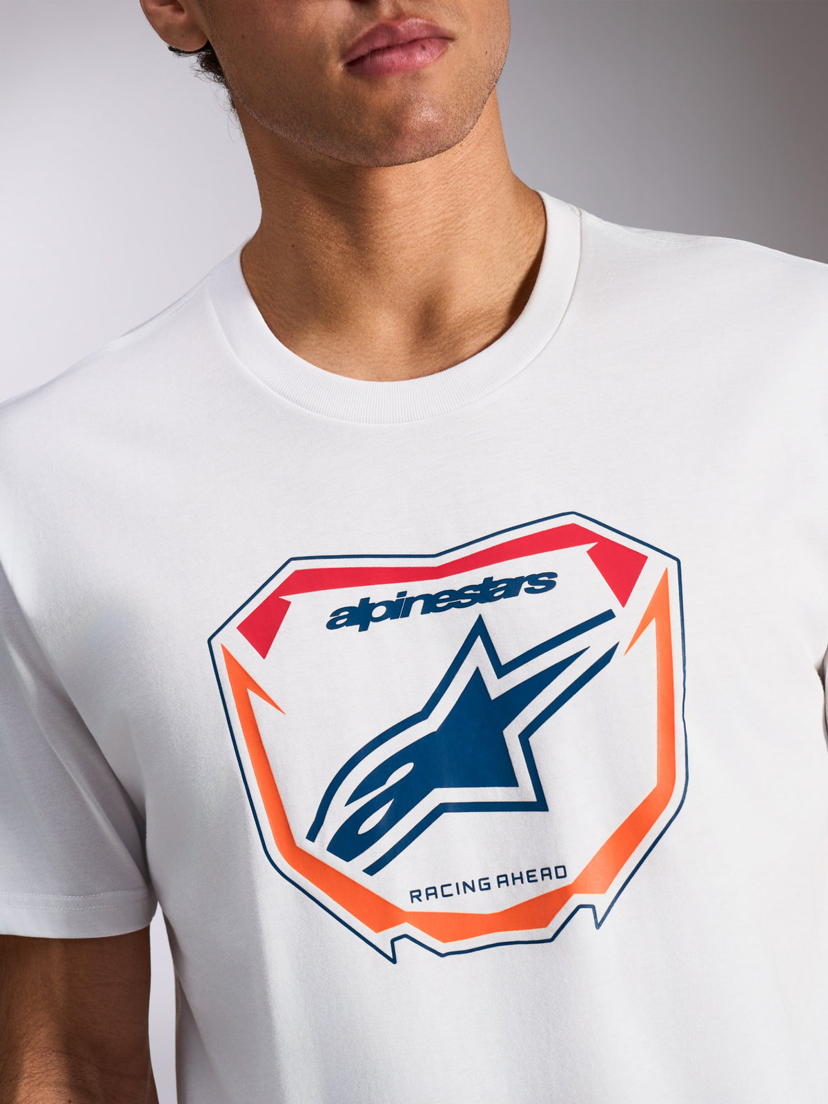 Alpinestars Plate CSF Tee, koszulka z krótkim rękawem, biała, grafika MX Plate z przodu z niebieskim logo Astars i napisem „Racing Ahead”, pomarańczowe i czerwone akcenty, codzienna odzież sportowa