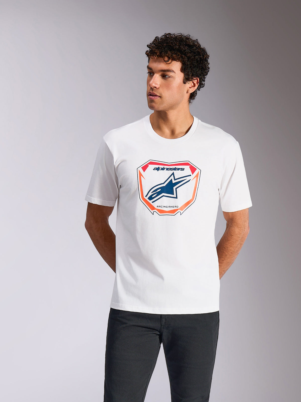 Alpinestars Plate CSF Tee, biała koszulka z krótkim rękawem, z grafiką płyty Astars MX na przodzie, niebieskim logo i pomarańczowym obramowaniem, prezentowana na modelu, codzienna odzież motorsportowa