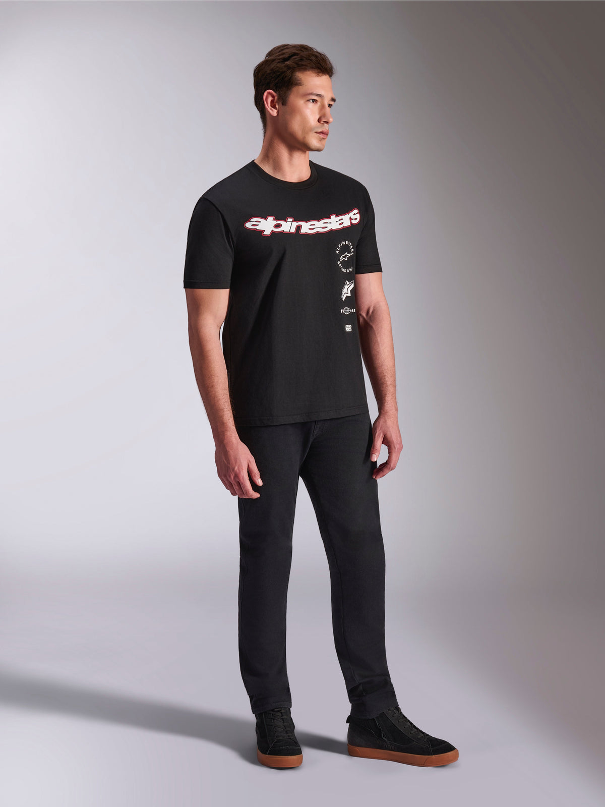 Alpinestars Abus CSF Tee, Short Sleeve T-Shirt, Black, featuring curved red and white Alpinestars logo with vertical stacked graphics, worn with black pants and sneakers, casual motorsport-inspired streetwear